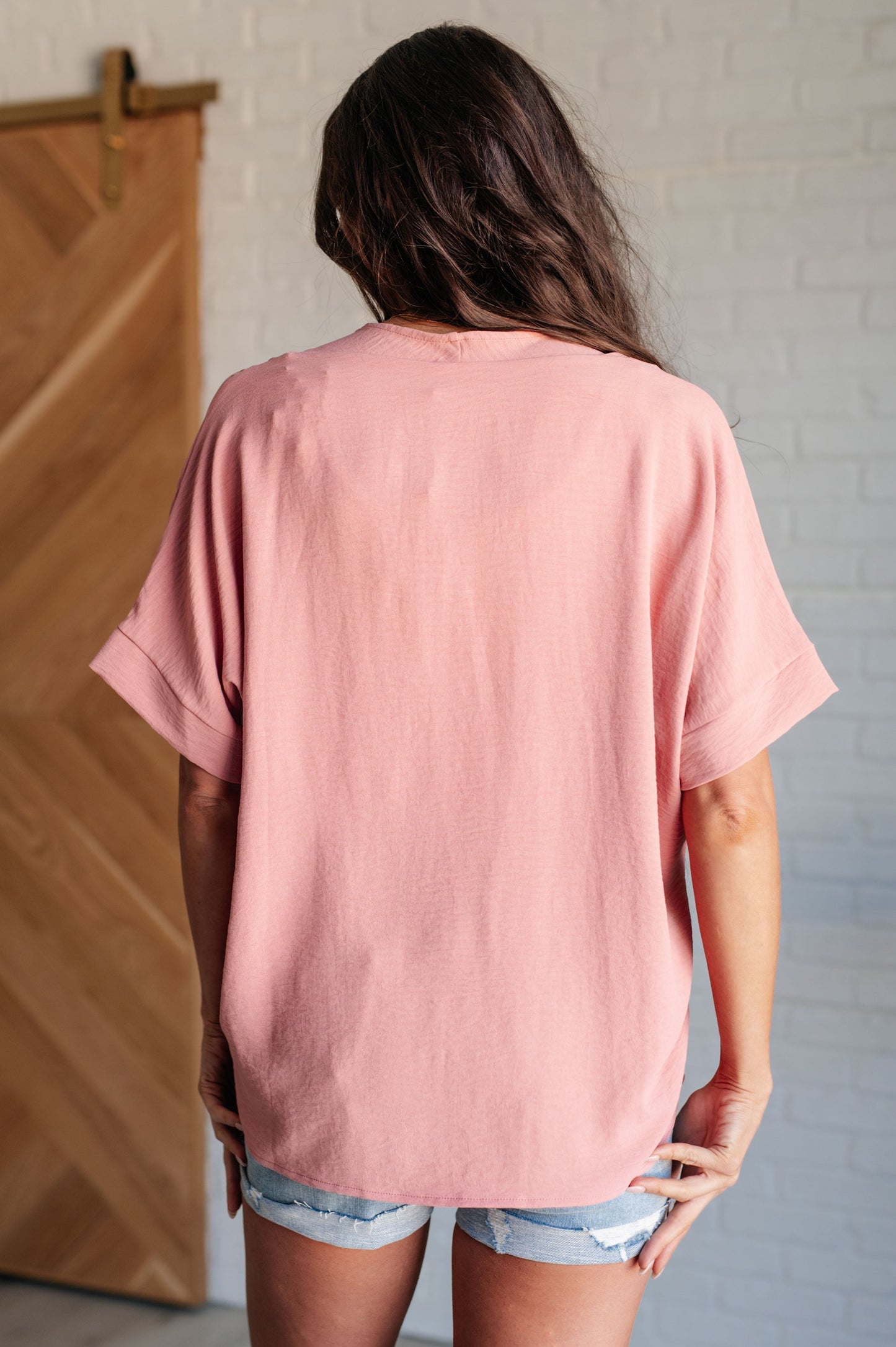 A blush-colored blouse with a V-neckline and relaxed fit. It has dolman short sleeves with banded cuffs, made from crinkle woven fabric for a stylish, easy look.