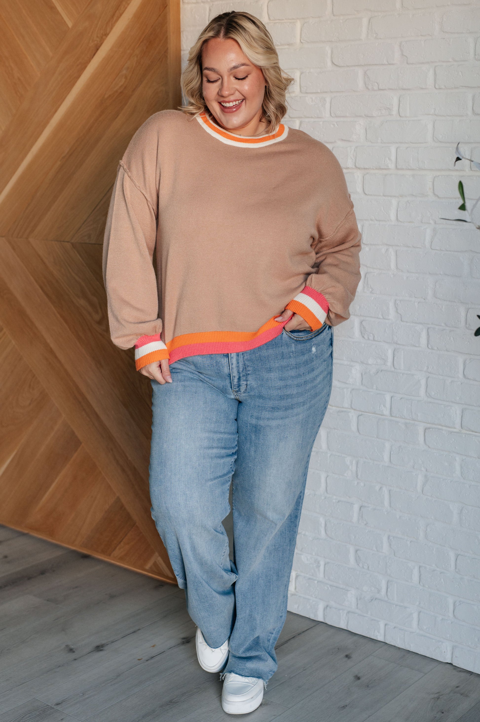 Women's beige sweater with orange, pink, and white accents, featuring a ribbed crew neckline, drop shoulders, banded cuffs, high-low hemline with side slits, and raw seam details.