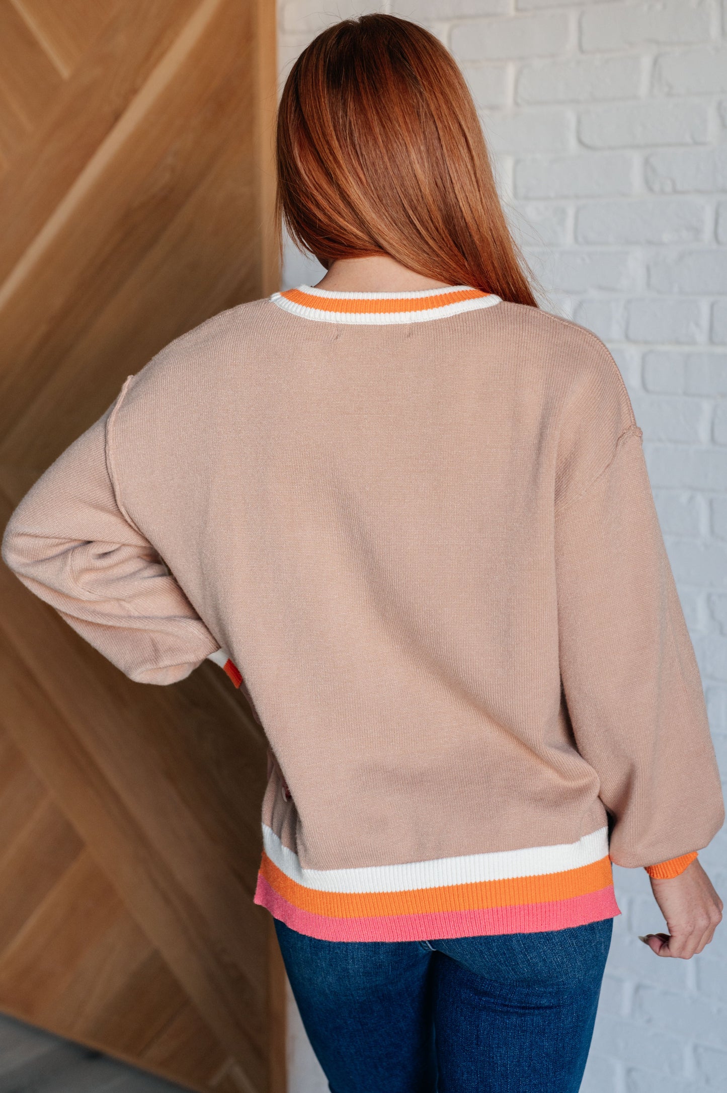 Women's beige sweater with orange, pink, and white accents, featuring a ribbed crew neckline, drop shoulders, banded cuffs, high-low hemline with side slits, and raw seam details.