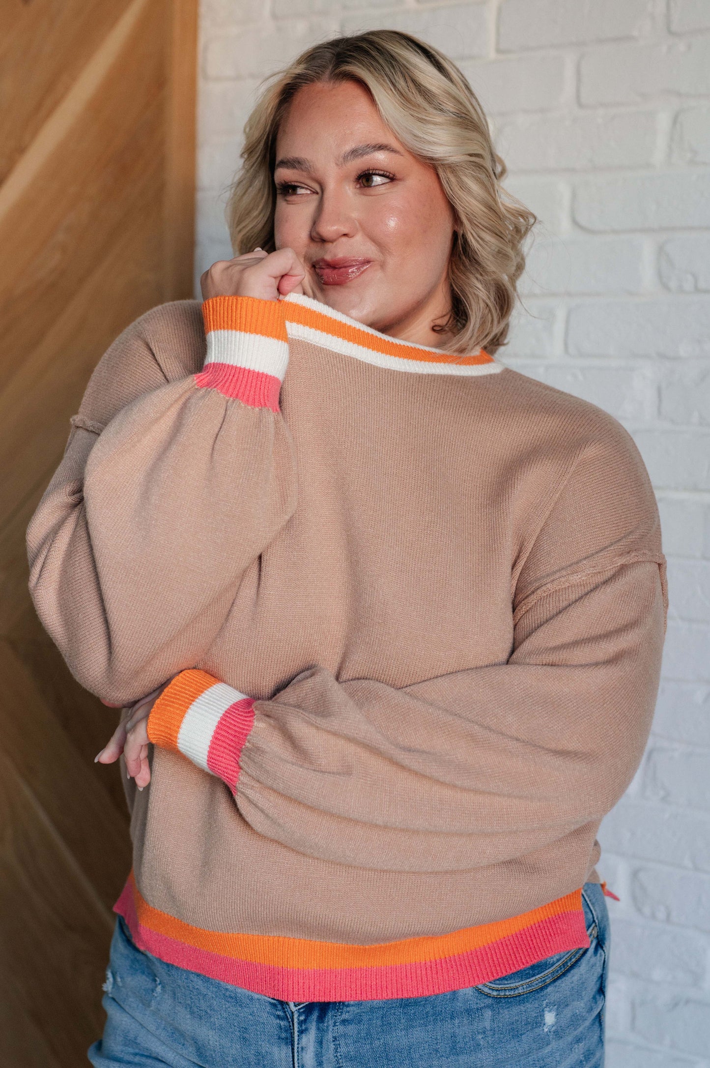 Women's beige sweater with orange, pink, and white accents, featuring a ribbed crew neckline, drop shoulders, banded cuffs, high-low hemline with side slits, and raw seam details.