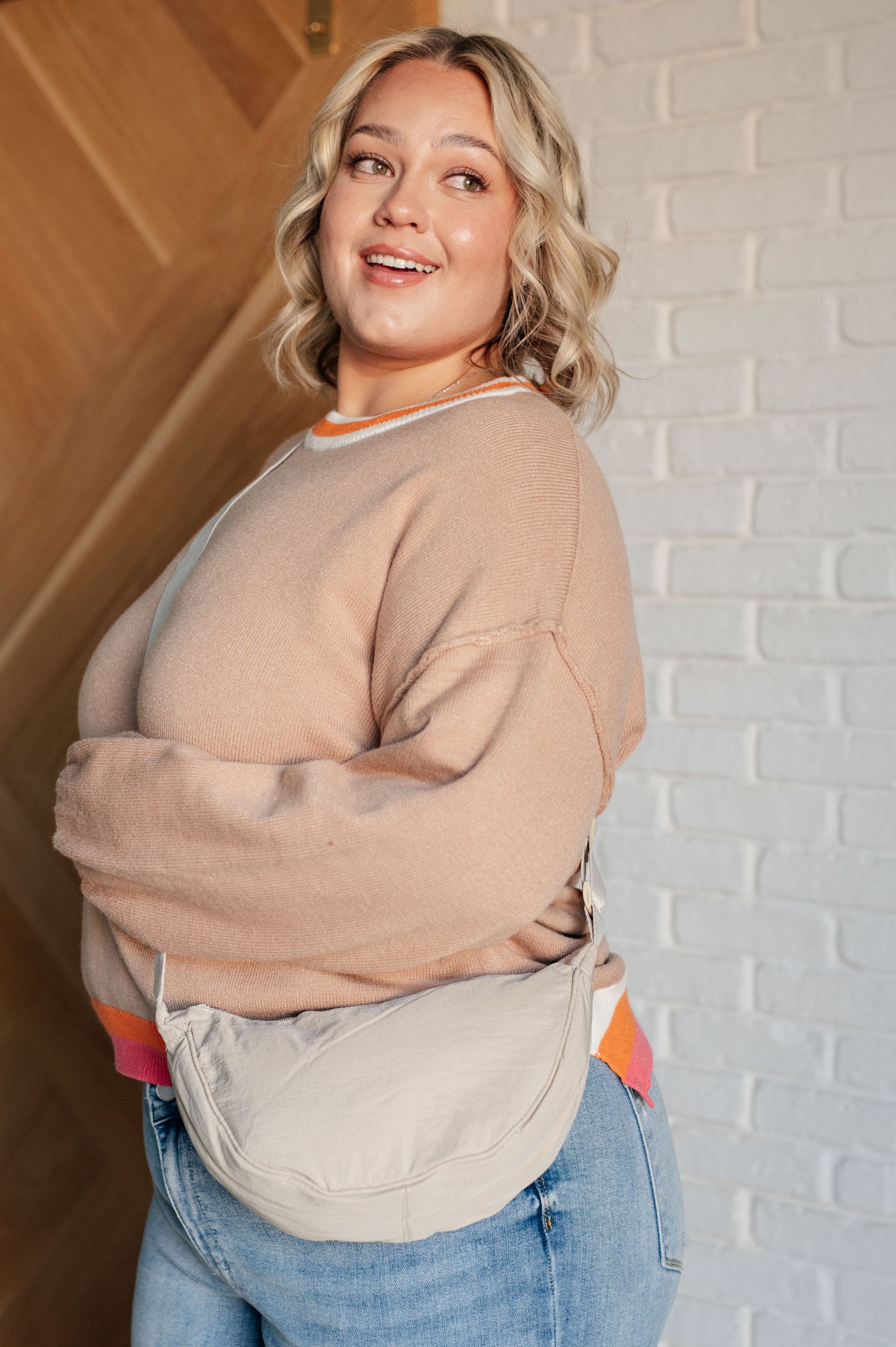 Women's beige sweater with orange, pink, and white accents, featuring a ribbed crew neckline, drop shoulders, banded cuffs, high-low hemline with side slits, and raw seam details.