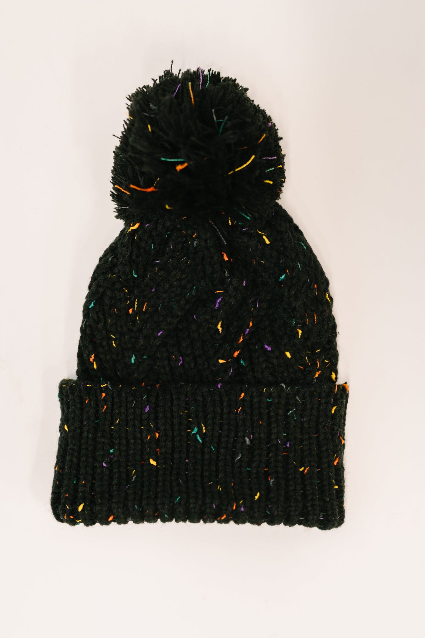 Flat lay of Cover Your Ears Pom Pom Beanie in black with cable knit and pom pom.