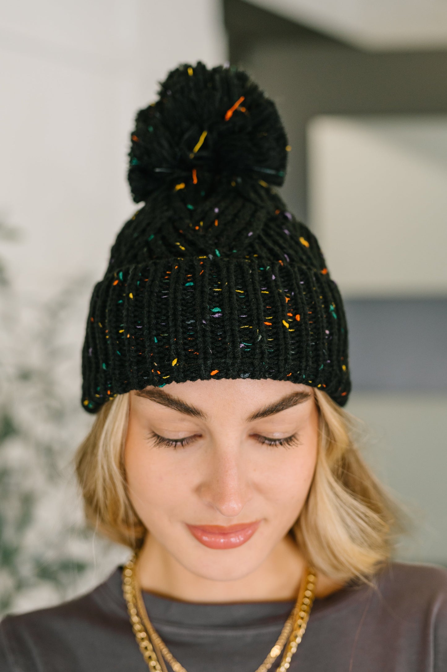 Model wearing Cover Your Ears Pom Pom Beanie in black speckled cable knit.