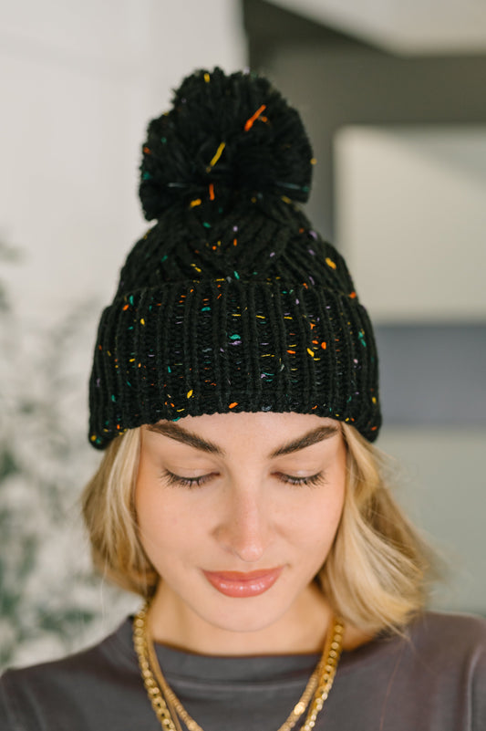 Model wearing Cover Your Ears Pom Pom Beanie in black speckled cable knit.