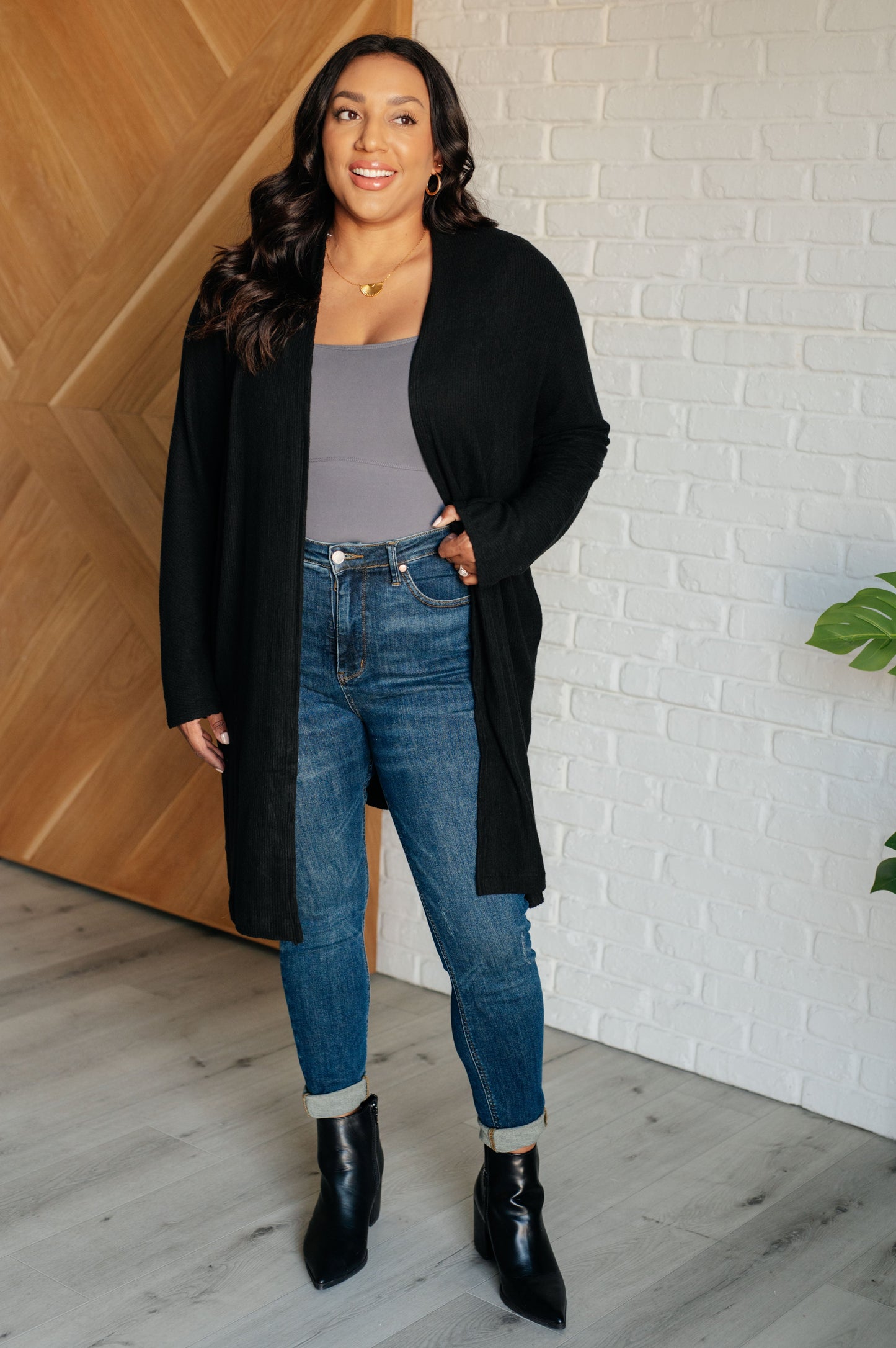 Black ribbed knit cardigan with a shawl neckline and long dolman sleeves. The open-front design features a long length, functional side pockets, and subtle side slits.