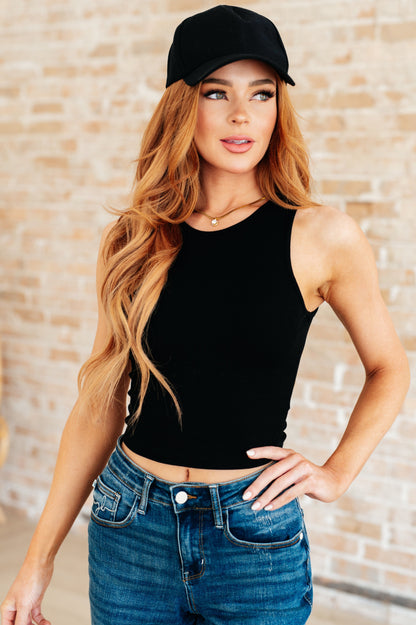 Woman wearing black rib knit crop tank top front view, round neckline, sleeveless summer layering essential.