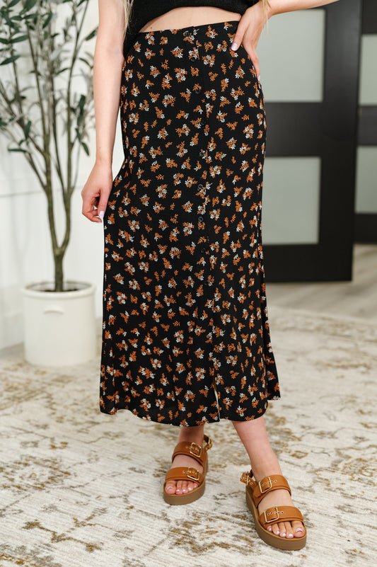 Front-facing view of the Luisa Midi Skirt in black with rust and white floral print, paired with sandals for a breezy, stylish look.
