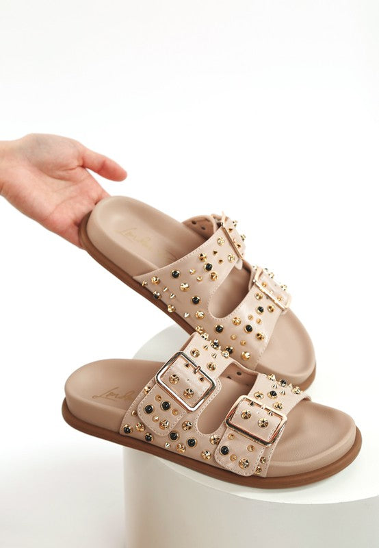 Beige studded sliders with metallic embellishments and double pin buckle straps – comfortable flat form sandals for casual and evening wear.