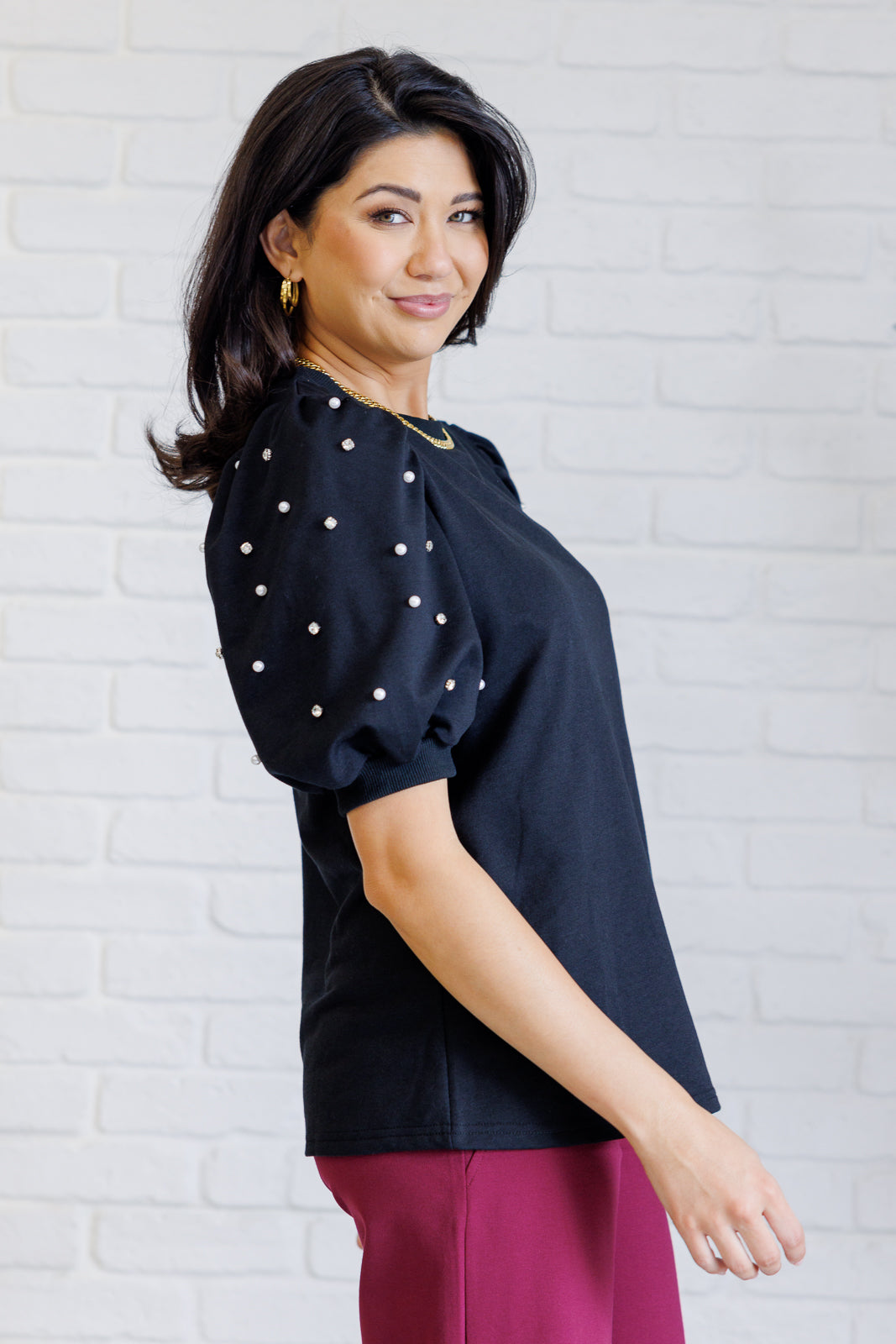 Black French terry top with a ribbed neckline, short balloon sleeves embellished with pearl and faux diamond accents, and ribbed sleeve cuffs.