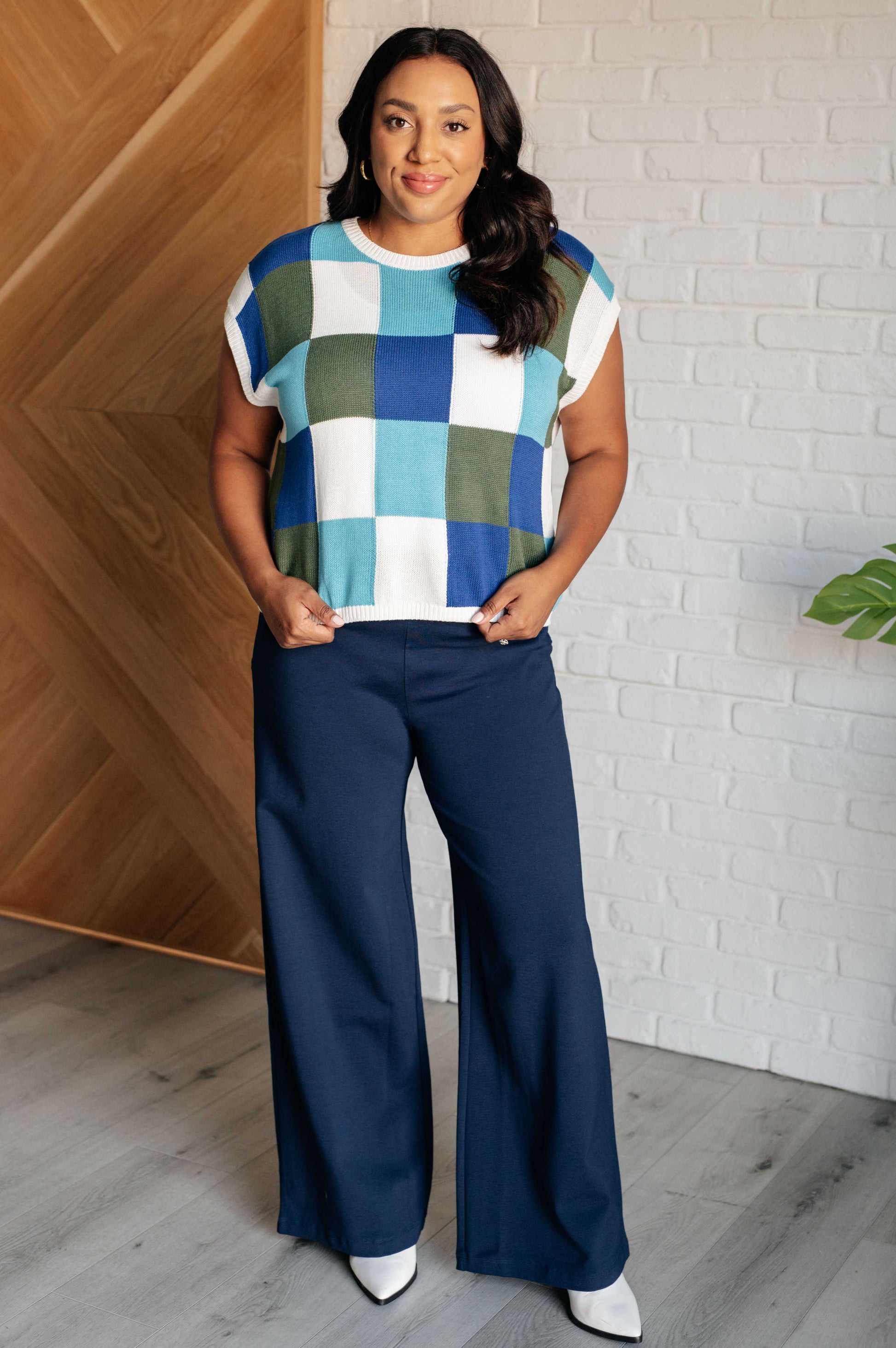 Women's sleeveless sweater in blue, green, and white checkered pattern. Made from sweater knit fabric with a ribbed round neckline, ribbed sleeve cuff, and hemline. Features a muscle tee silhouette.