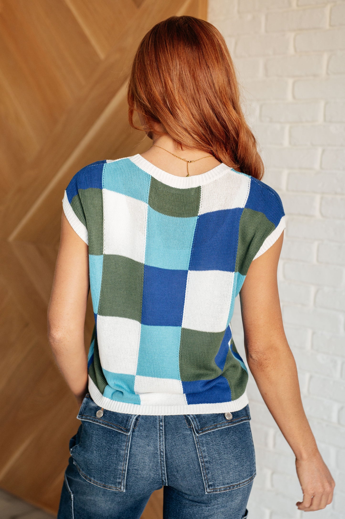 Women's sleeveless sweater in blue, green, and white checkered pattern. Made from sweater knit fabric with a ribbed round neckline, ribbed sleeve cuff, and hemline. Features a muscle tee silhouette.