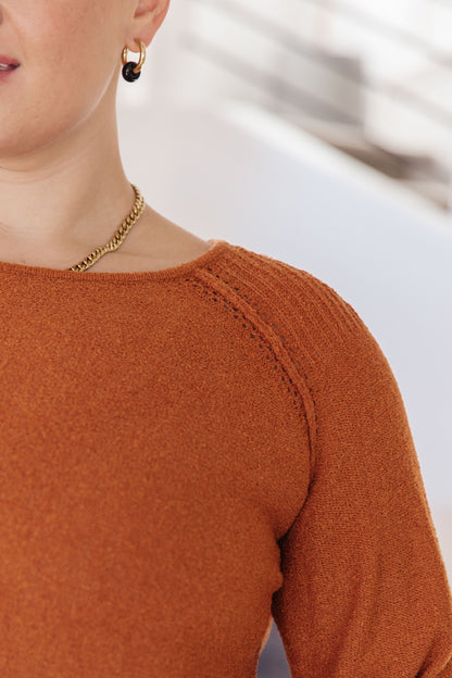 Close-up of rust sweater knit fabric with raglan seam and rolled hem finish