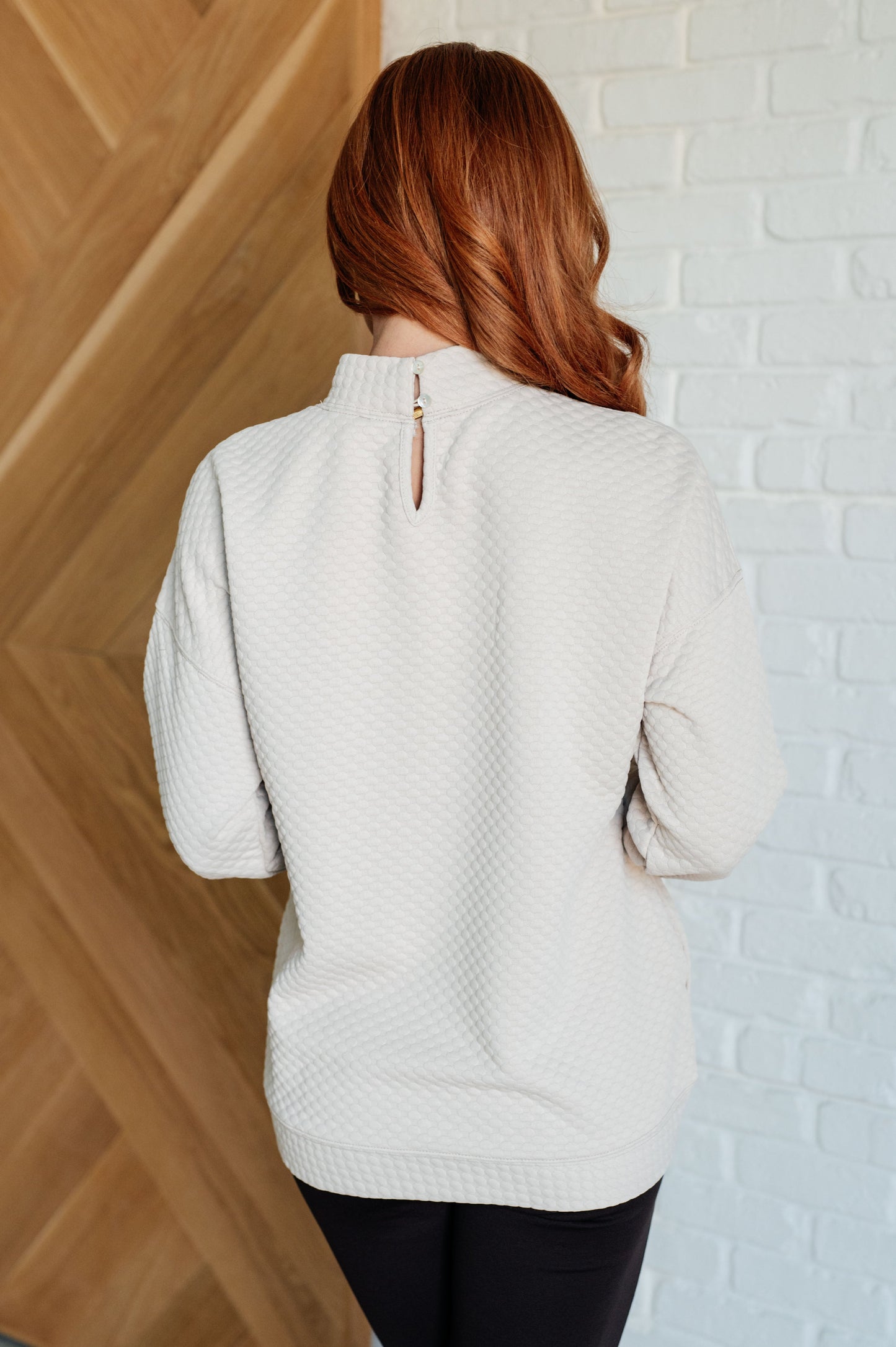 Cream textured knit pullover with a mock neckline, long sleeves, side seam pockets, and a banded hem. Relaxed fit with a keyhole button closure at the back.