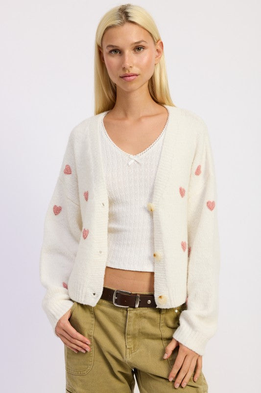 Model wearing Donna Cropped Cardigan in ivory with pink heart embroidery and V-neckline.