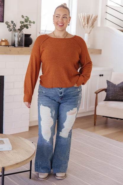Plus size model sitting in Dorothy Rust Sweater, cozy round neckline with exposed seams