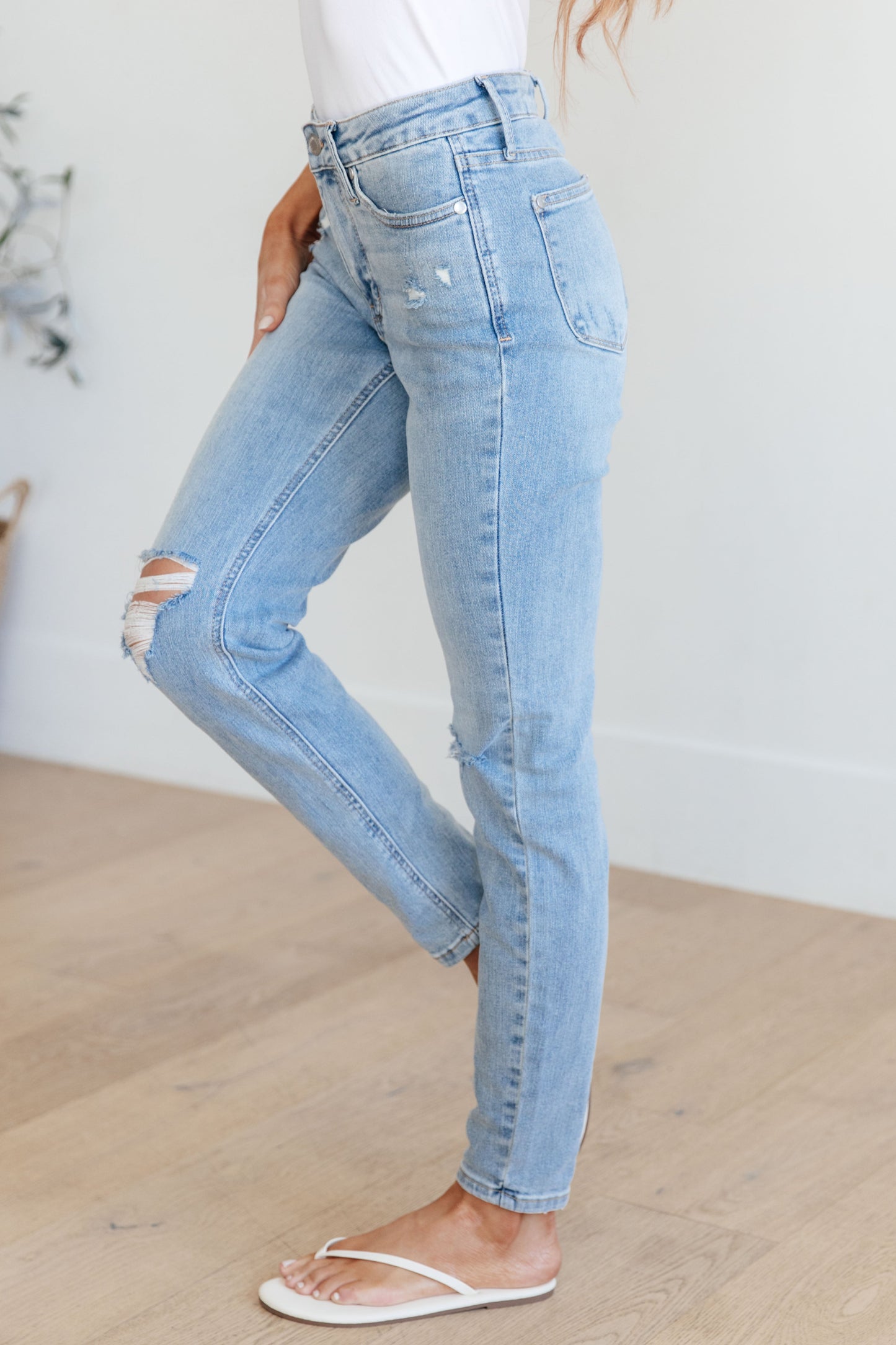 Light wash mid-rise skinny jeans with tummy control and 4-way stretch for comfort. Features distressed details and a zip fly closure.