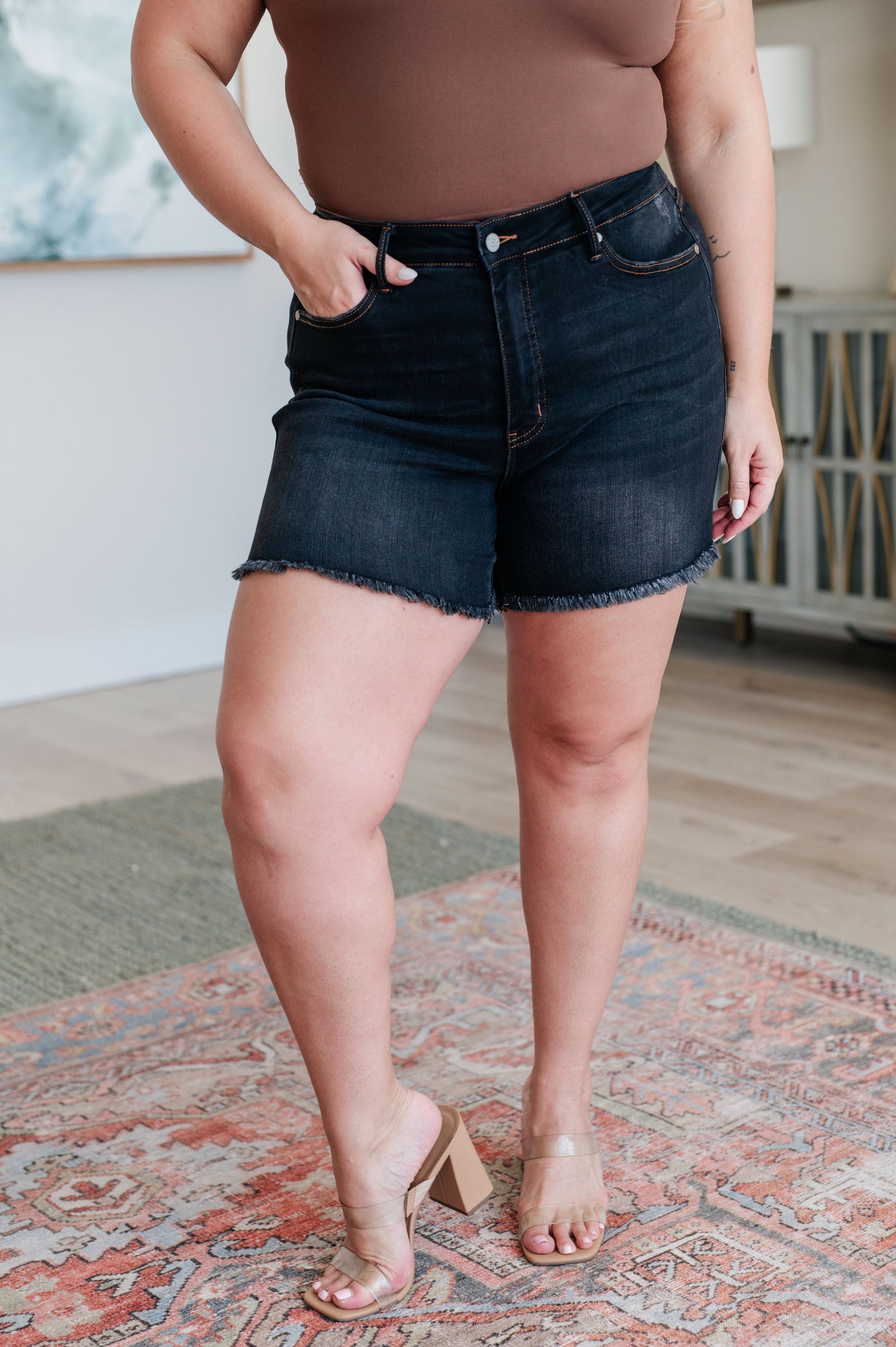 High-rise black denim shorts with tummy control and a raw frayed hem. Zip fly closure and casual style.