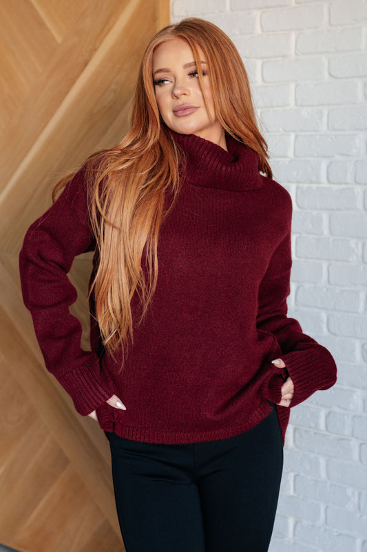 Dark red turtleneck sweater with drop shoulders, ribbed cuffs, and a split, stepped hem.