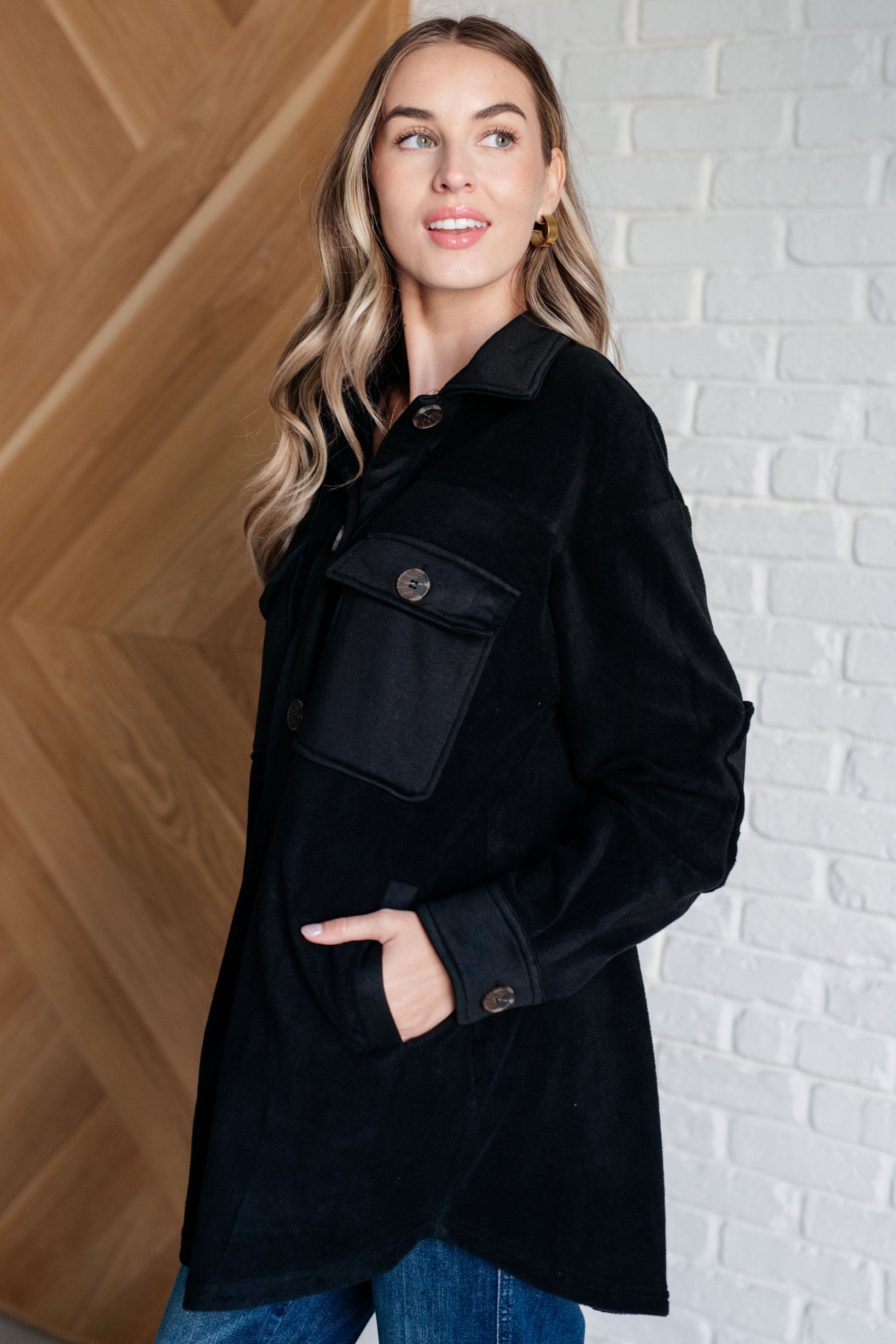 Black fleece jacket with a collared neckline, contrast panels, elbow patches, functional button closures, and banded sleeve cuffs. Features chest patch and side welt pockets.