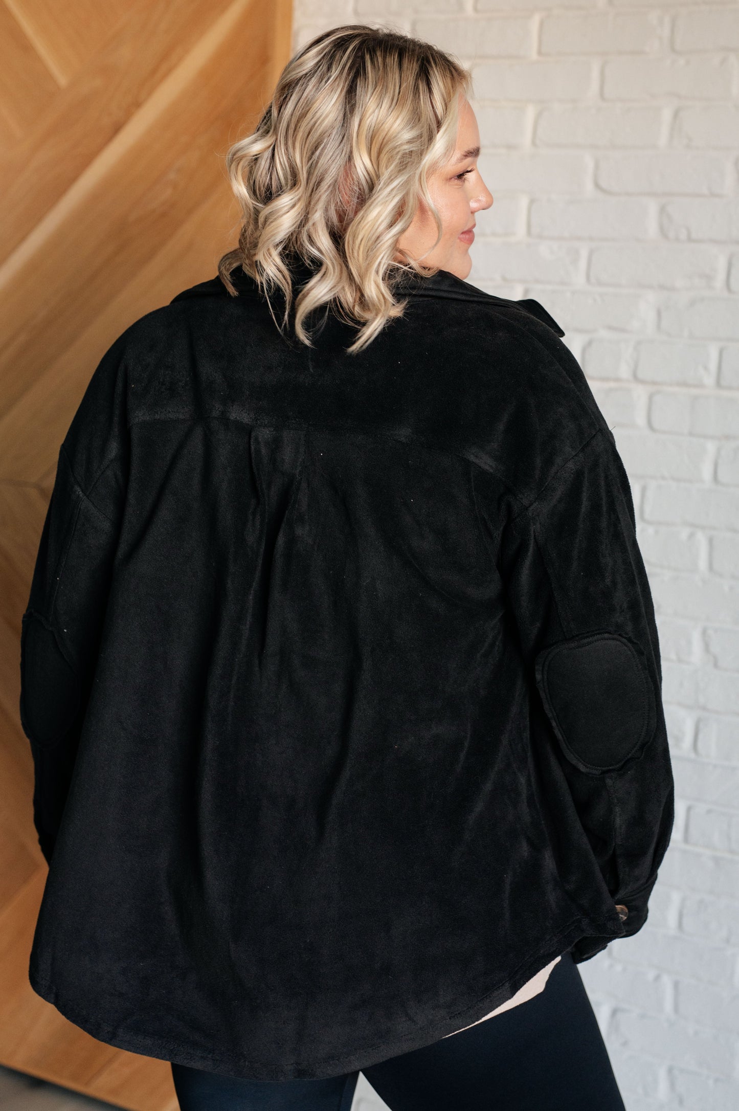 Black fleece jacket with a collared neckline, contrast panels, elbow patches, functional button closures, and banded sleeve cuffs. Features chest patch and side welt pockets.