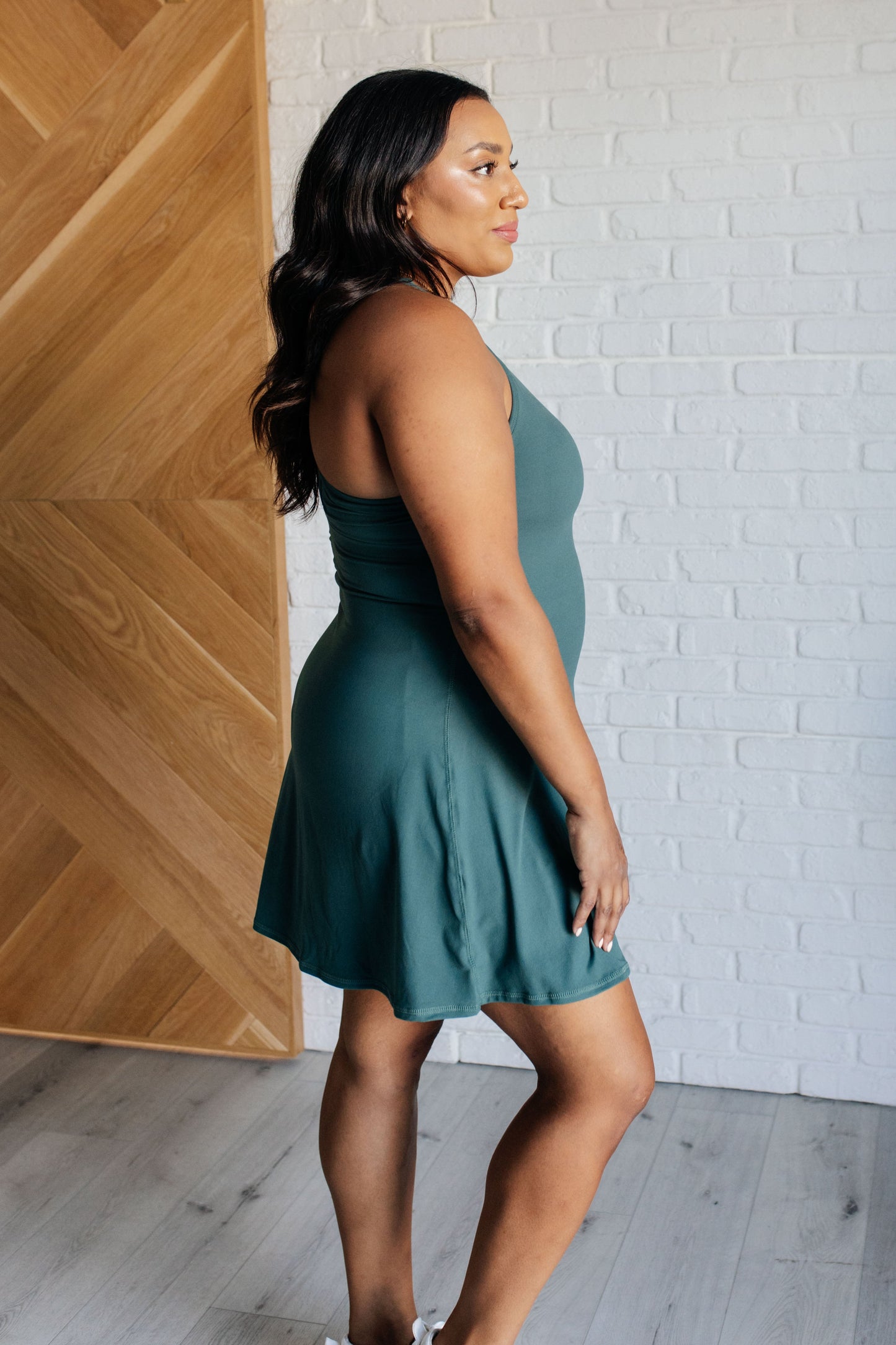 Everglade green tennis style dress with a scoop neckline, back cutouts, built-in bra with removable cups, skort design, and functional pockets.