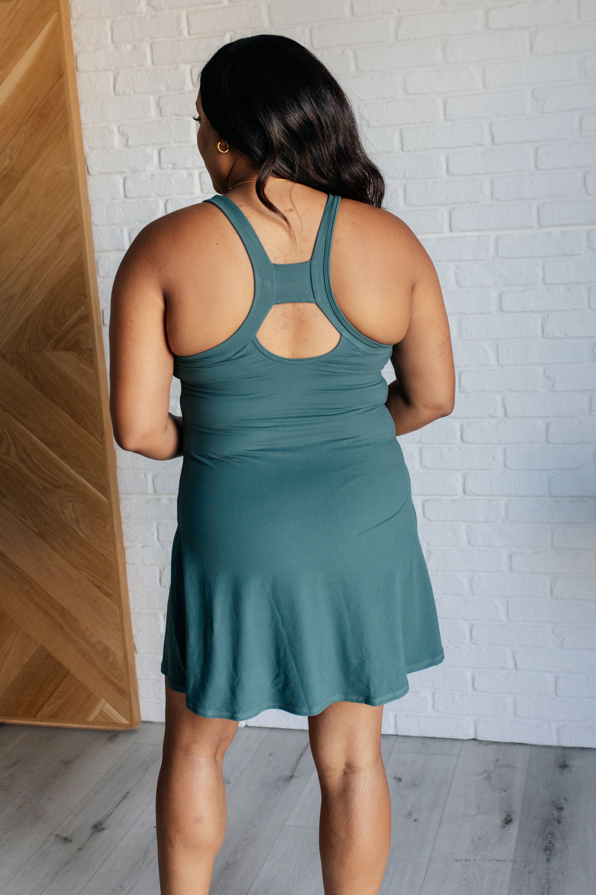 Everglade green tennis style dress with a scoop neckline, back cutouts, built-in bra with removable cups, skort design, and functional pockets.