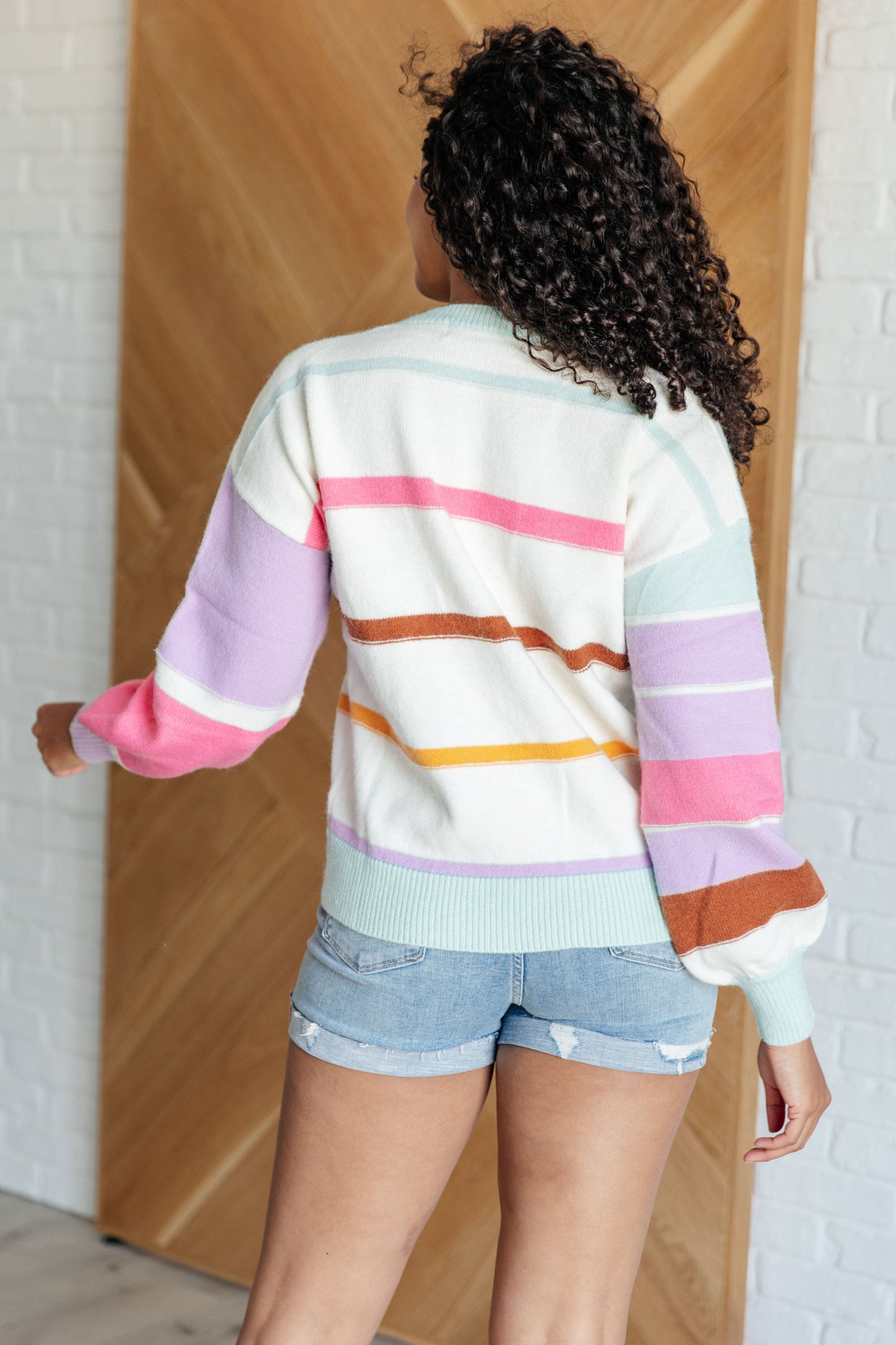 Women's multi-colored striped sweater made from lightweight sweater knit. With a ribbed rounded neckline, long balloon sleeves with drop shoulder, and ribbed sleeve cuffs and hemline.