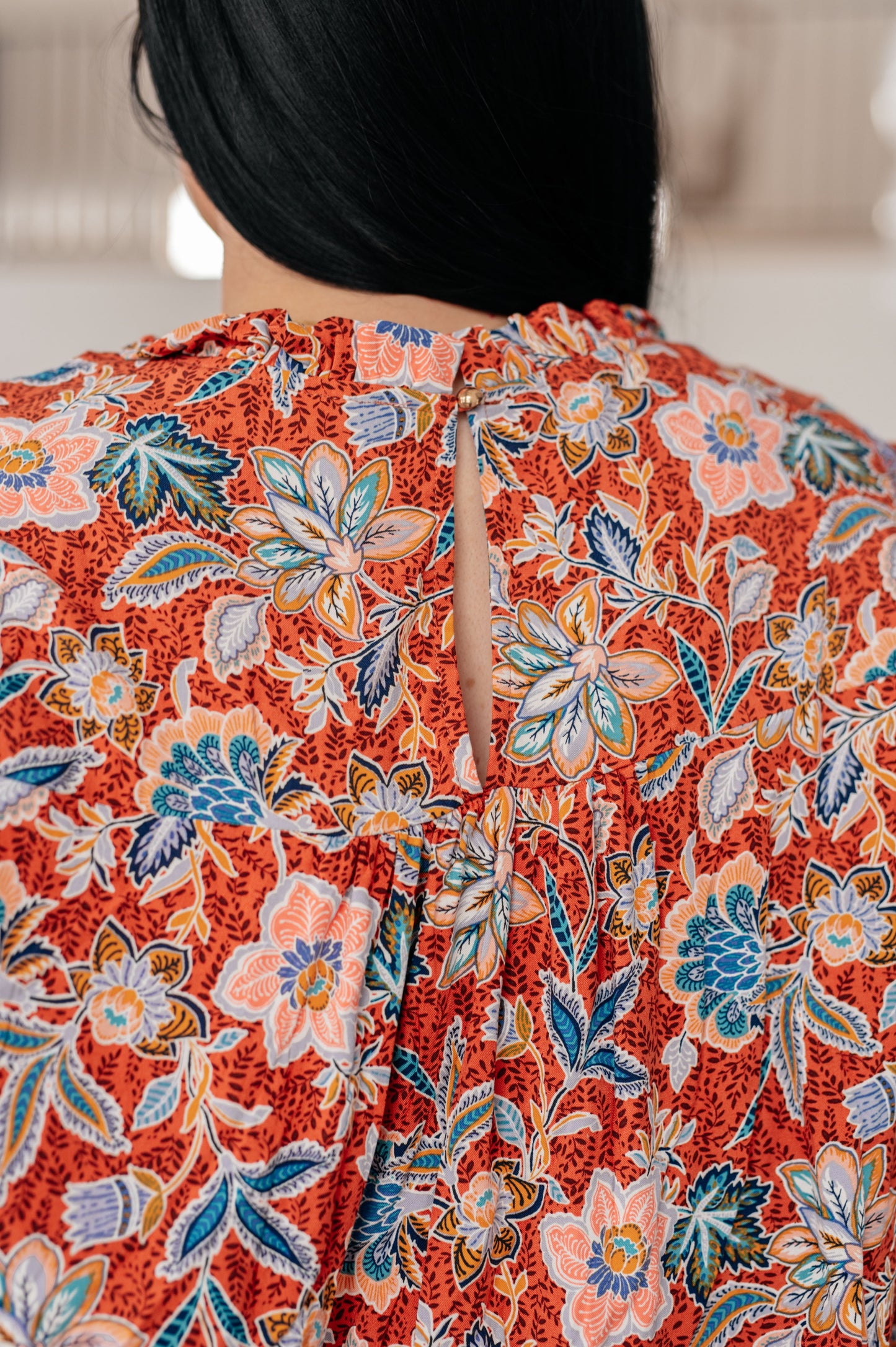 Close-up of Blair Floral Blouse keyhole button closure with ruffled neckline detail in rust floral fabric