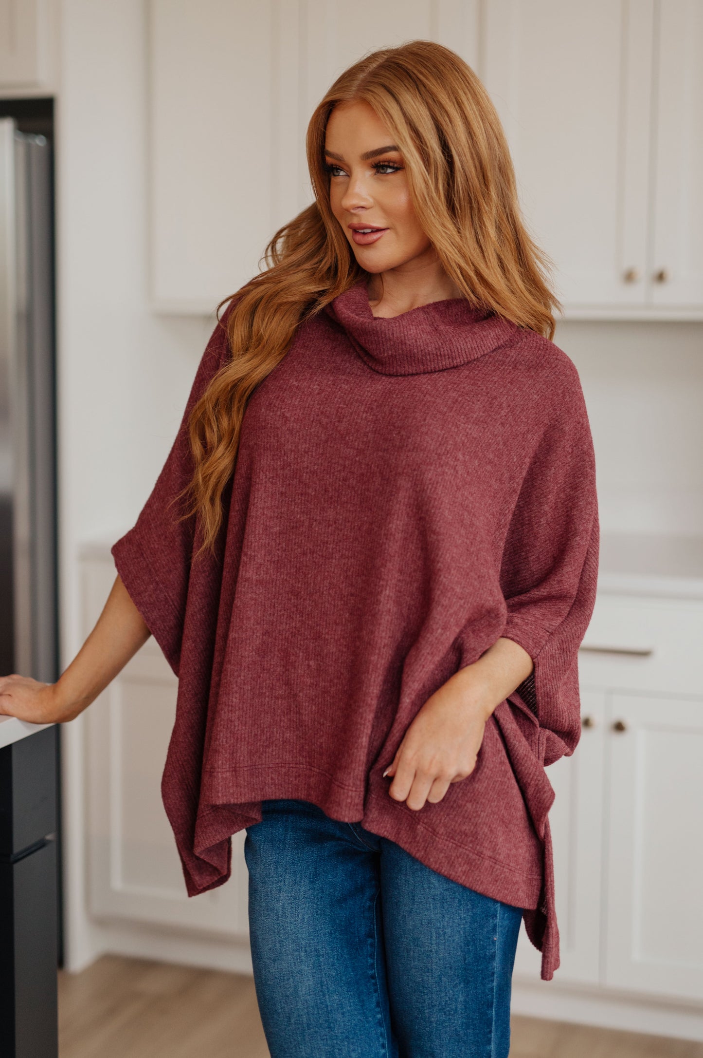 Women's dark mauve poncho made from brushed ribbed hacci knit fabric, featuring a cowl neckline, poncho silhouette, side slit, and a relaxed fit.