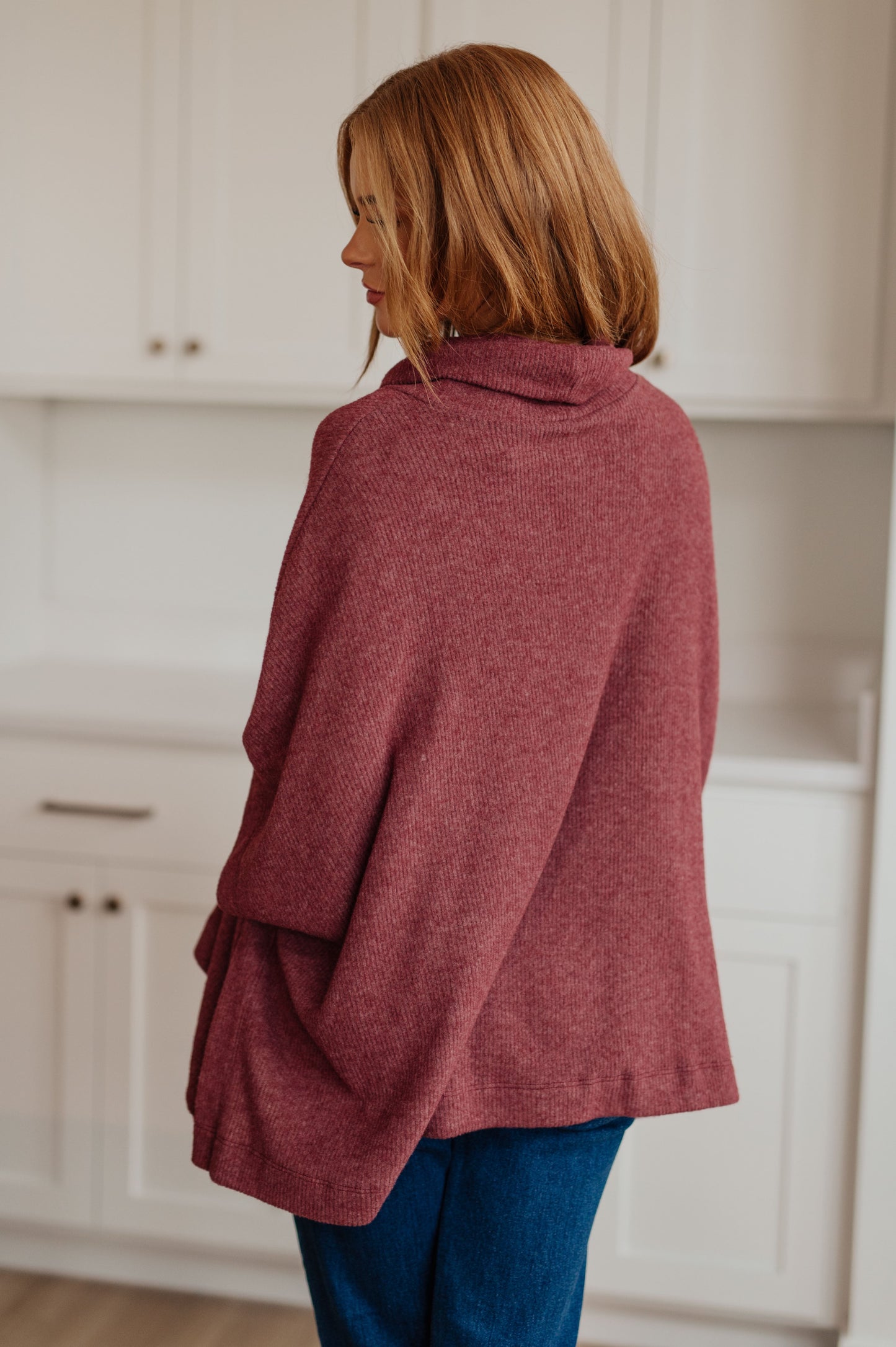 Women's dark mauve poncho made from brushed ribbed hacci knit fabric, featuring a cowl neckline, poncho silhouette, side slit, and a relaxed fit.