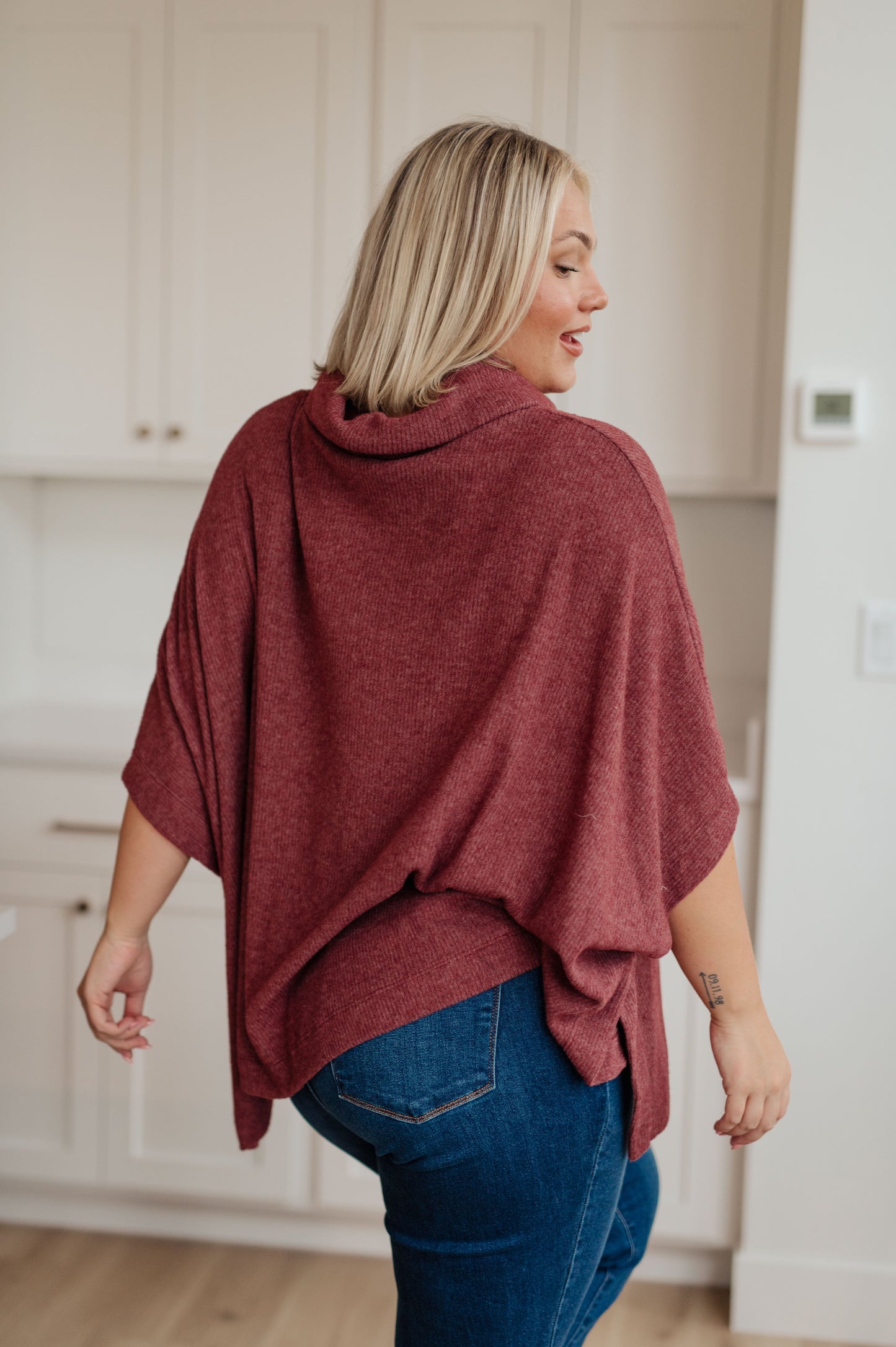 Women's dark mauve poncho made from brushed ribbed hacci knit fabric, featuring a cowl neckline, poncho silhouette, side slit, and a relaxed fit.