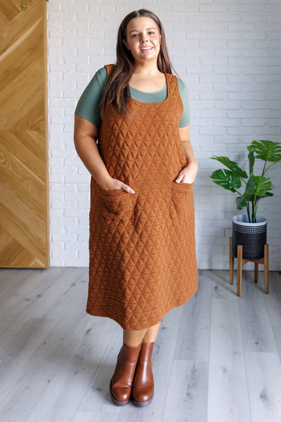 Caramel quilted knit jumper-style midi dress with a scoop neckline, sleeveless design, A-line fit, and patch pockets.