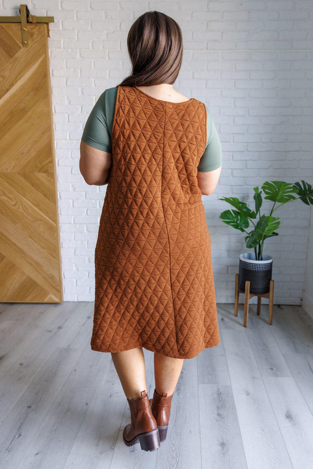 Caramel quilted knit jumper-style midi dress with a scoop neckline, sleeveless design, A-line fit, and patch pockets.