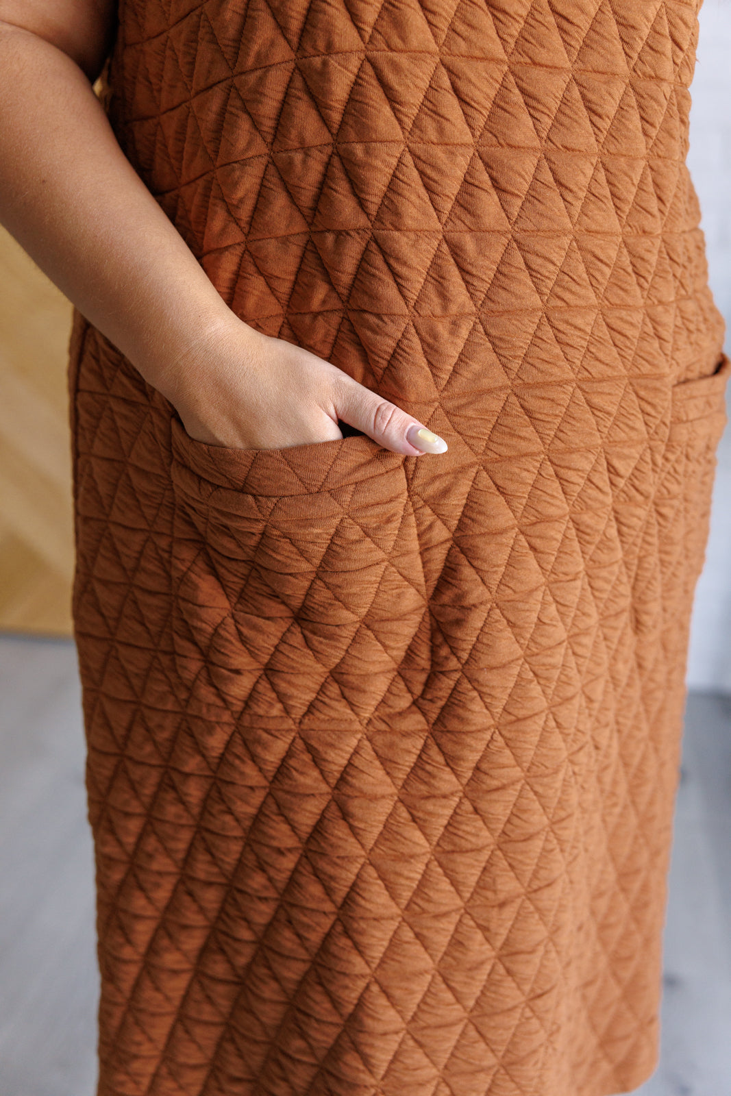 Caramel quilted knit jumper-style midi dress with a scoop neckline, sleeveless design, A-line fit, and patch pockets.