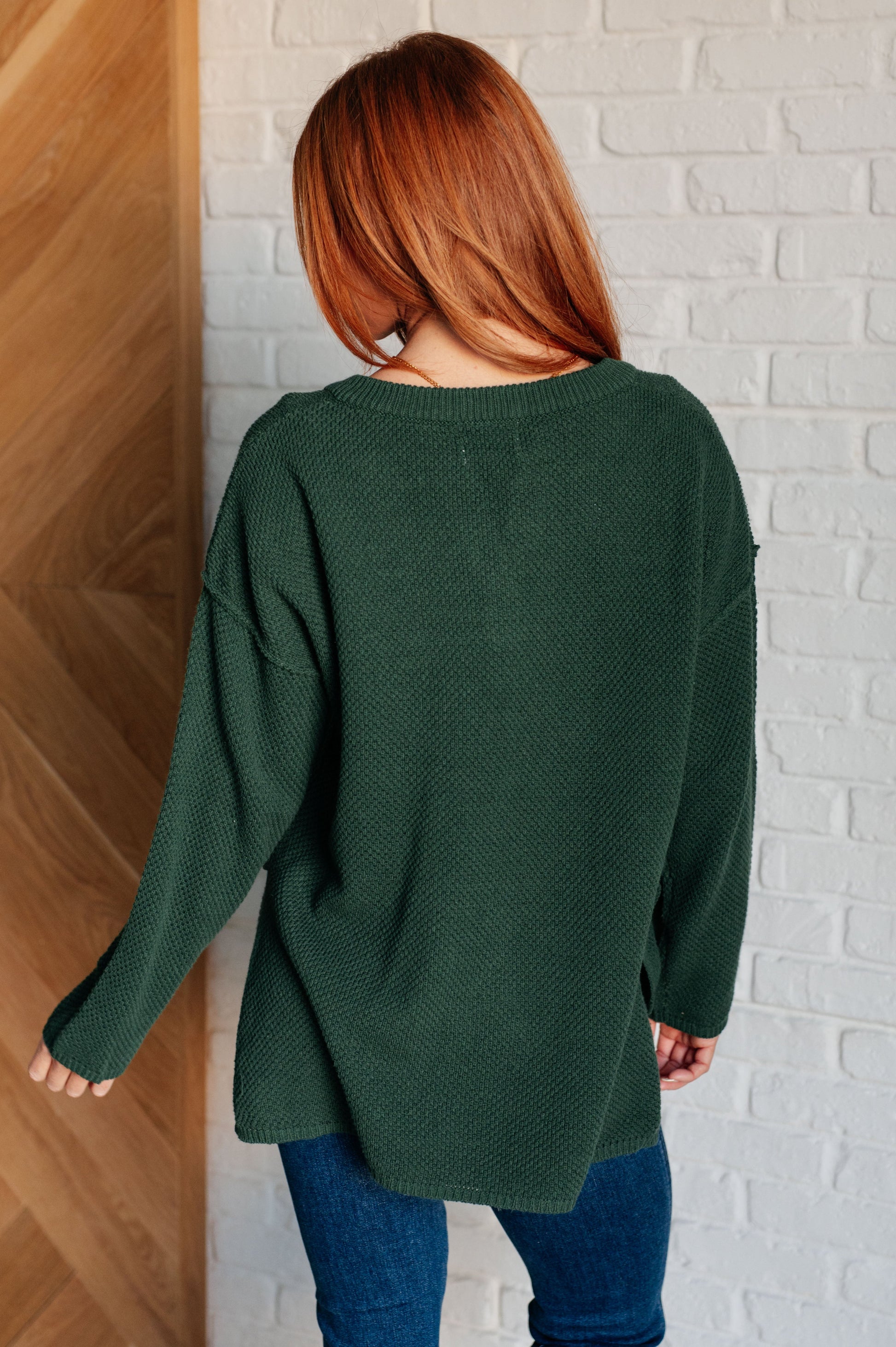 Women's dark green henley sweater with a ribbed button-up neckline, exposed seams, long sleeves, and a stepped hem with side slits.