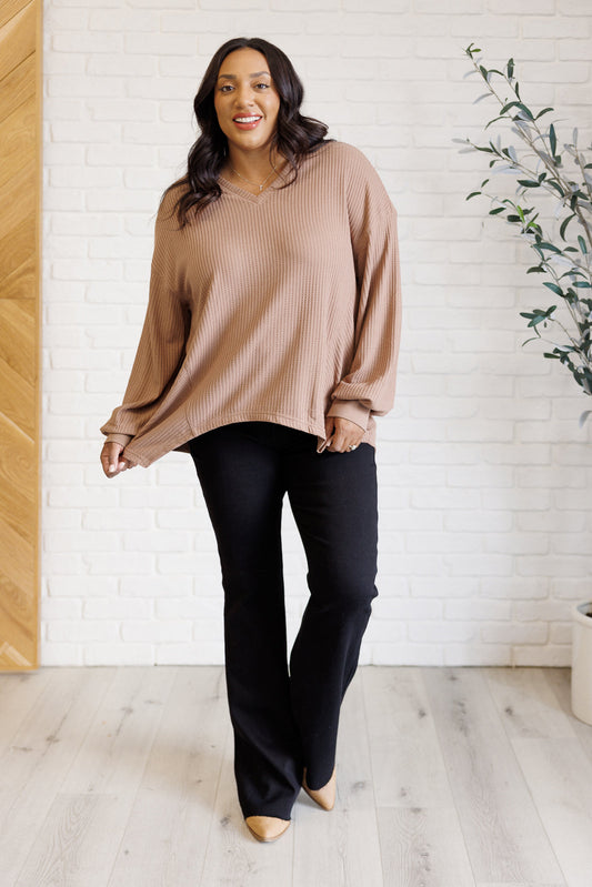 Women's coffee-colored waffle knit top with a V-neckline, long sleeves, banded sleeve cuffs, faux tag detail, and a scooped asymmetrical hemline.