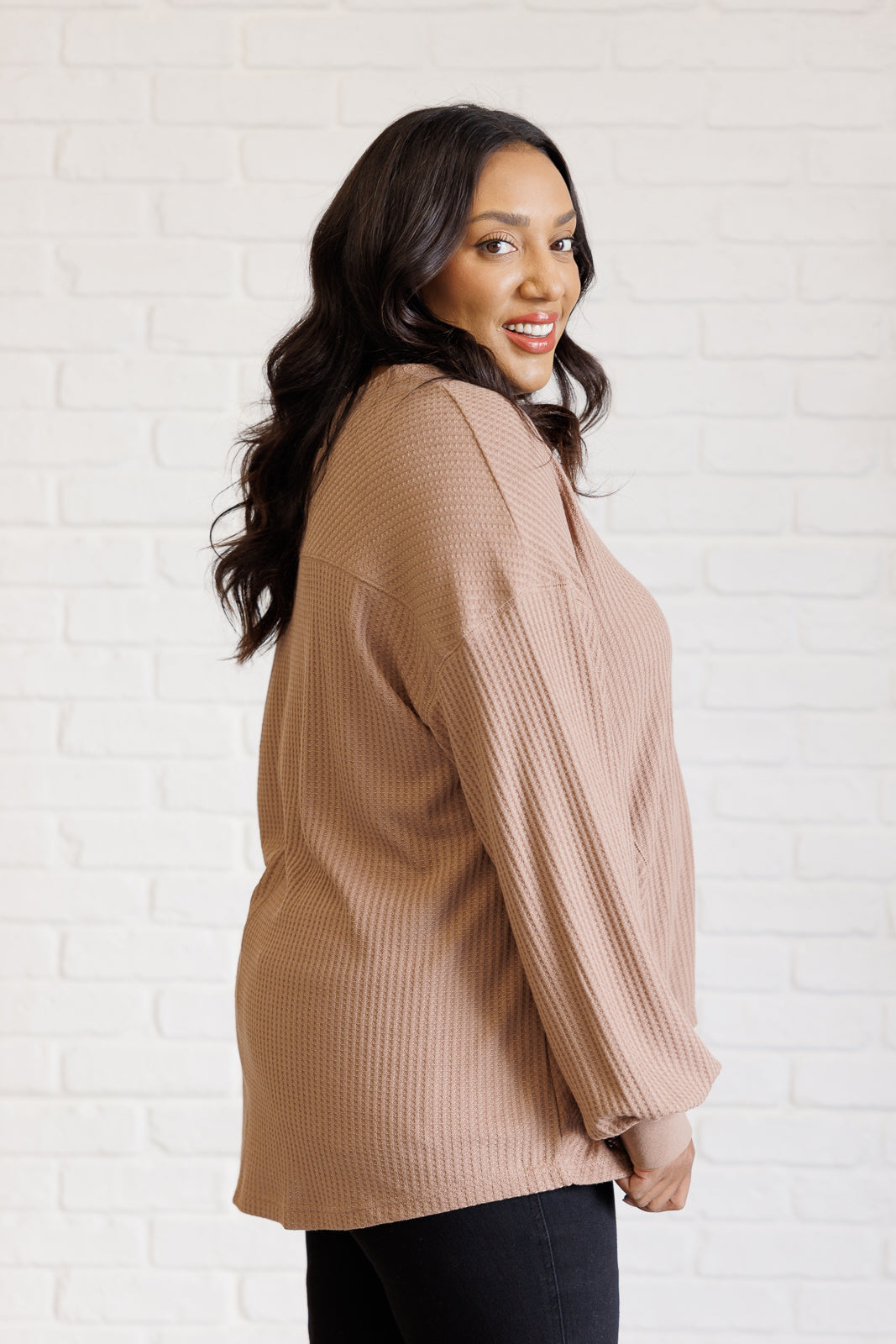 Women's coffee-colored waffle knit top with a V-neckline, long sleeves, banded sleeve cuffs, faux tag detail, and a scooped asymmetrical hemline.