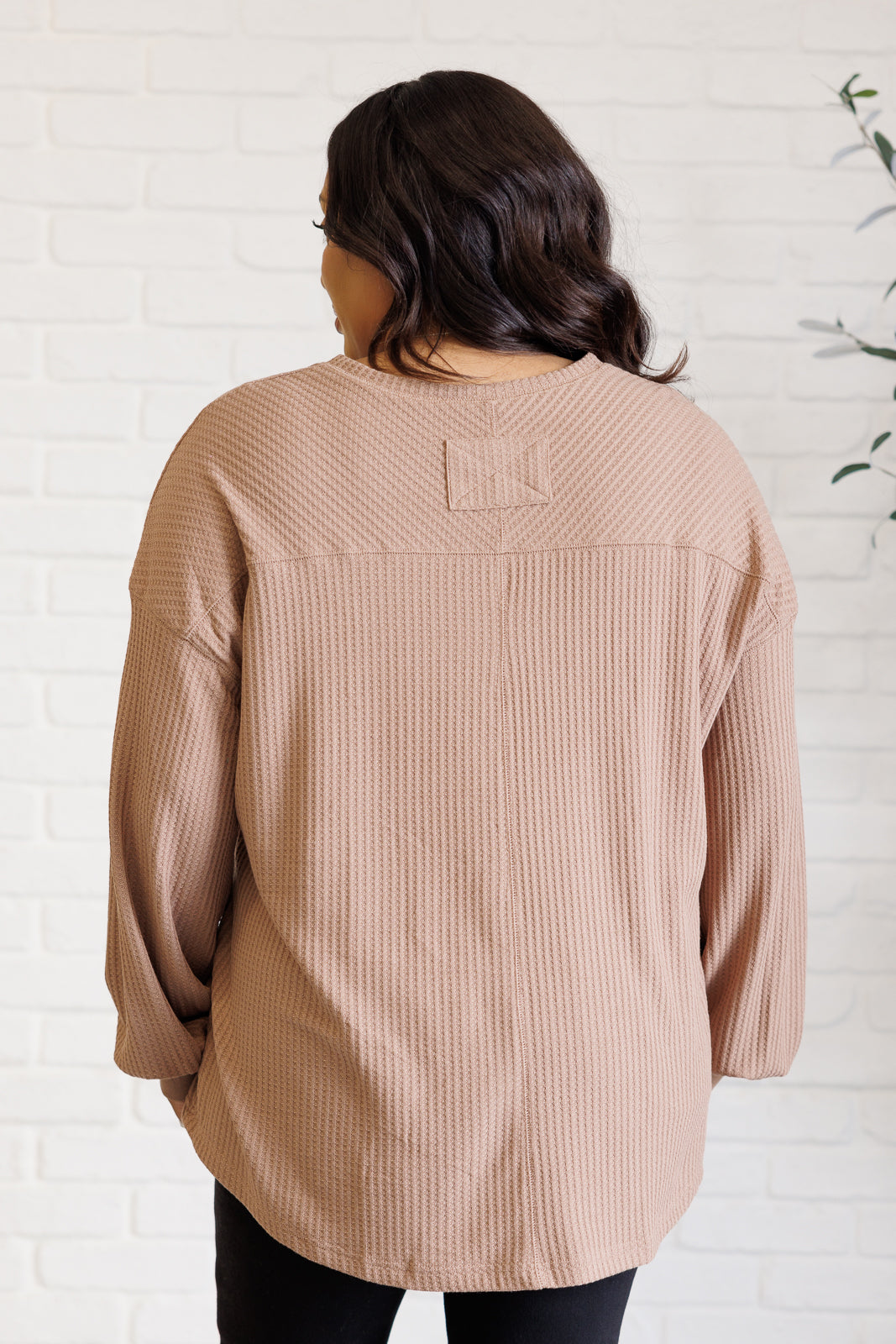 Women's coffee-colored waffle knit top with a V-neckline, long sleeves, banded sleeve cuffs, faux tag detail, and a scooped asymmetrical hemline.