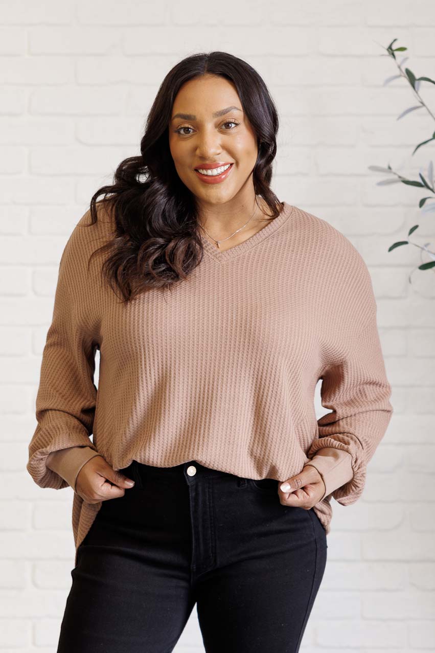 Women's coffee-colored waffle knit top with a V-neckline, long sleeves, banded sleeve cuffs, faux tag detail, and a scooped asymmetrical hemline.