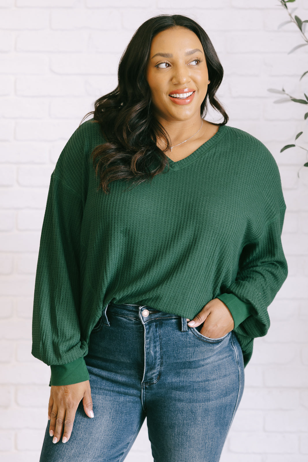 Women's green waffle knit top with a V-neckline, long sleeves, banded sleeve cuffs, faux tag detail, and a scooped asymmetrical hemline.