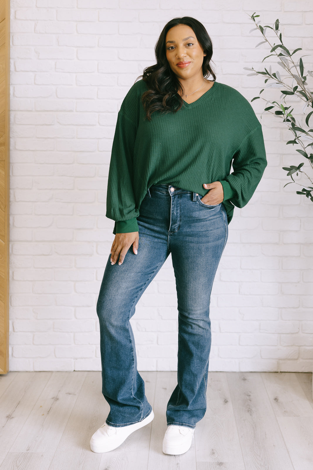 Women's green waffle knit top with a V-neckline, long sleeves, banded sleeve cuffs, faux tag detail, and a scooped asymmetrical hemline.