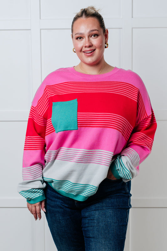 Midweight striped sweater in pink, red, white, and blue. Features a banded ribbed round neckline, long sleeves with drop shoulders, and a functional patch pocket. Banded ribbed cuffs and hem, with an oversized fit.