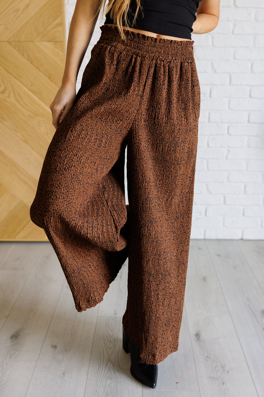 High-rise wide-leg pants in brown with a polka dot print, smocked elastic waistband, textured fabric, and pockets.