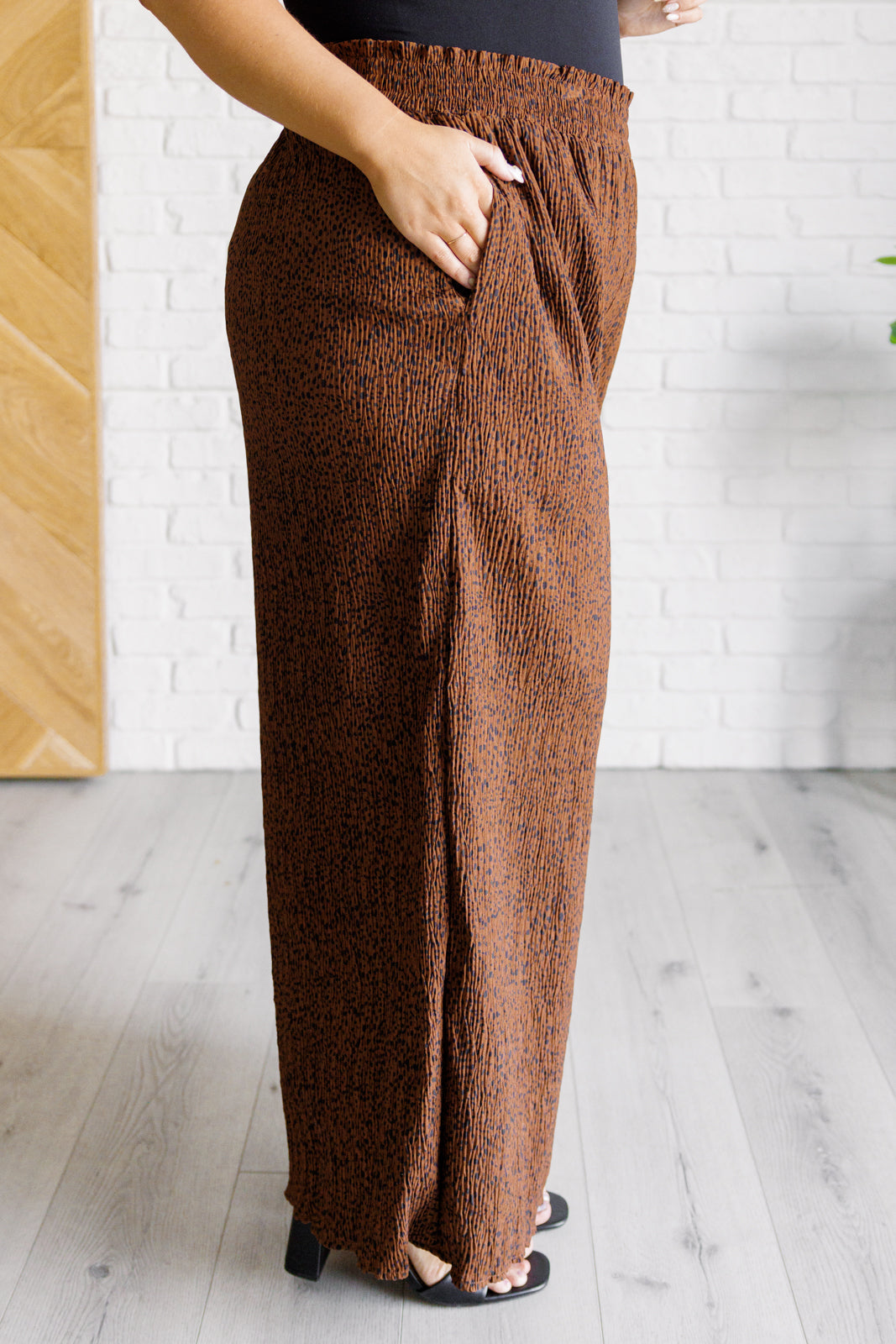 Plus size, high-rise wide-leg pants in brown with a polka dot print, smocked elastic waistband, textured fabric, and pockets.