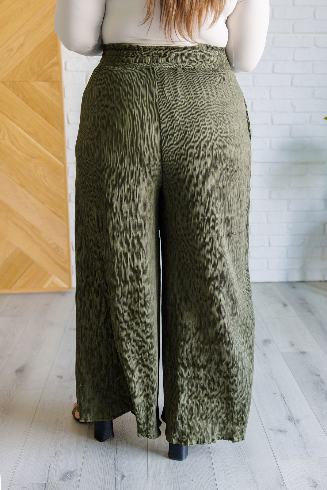 High Rise Wide Leg Pants in olive with a smocked elastic waistband, textured crinkle woven fabric, and subtle polka dot print. Featuring a wide-leg silhouette and functional pockets for a chic, standout look.