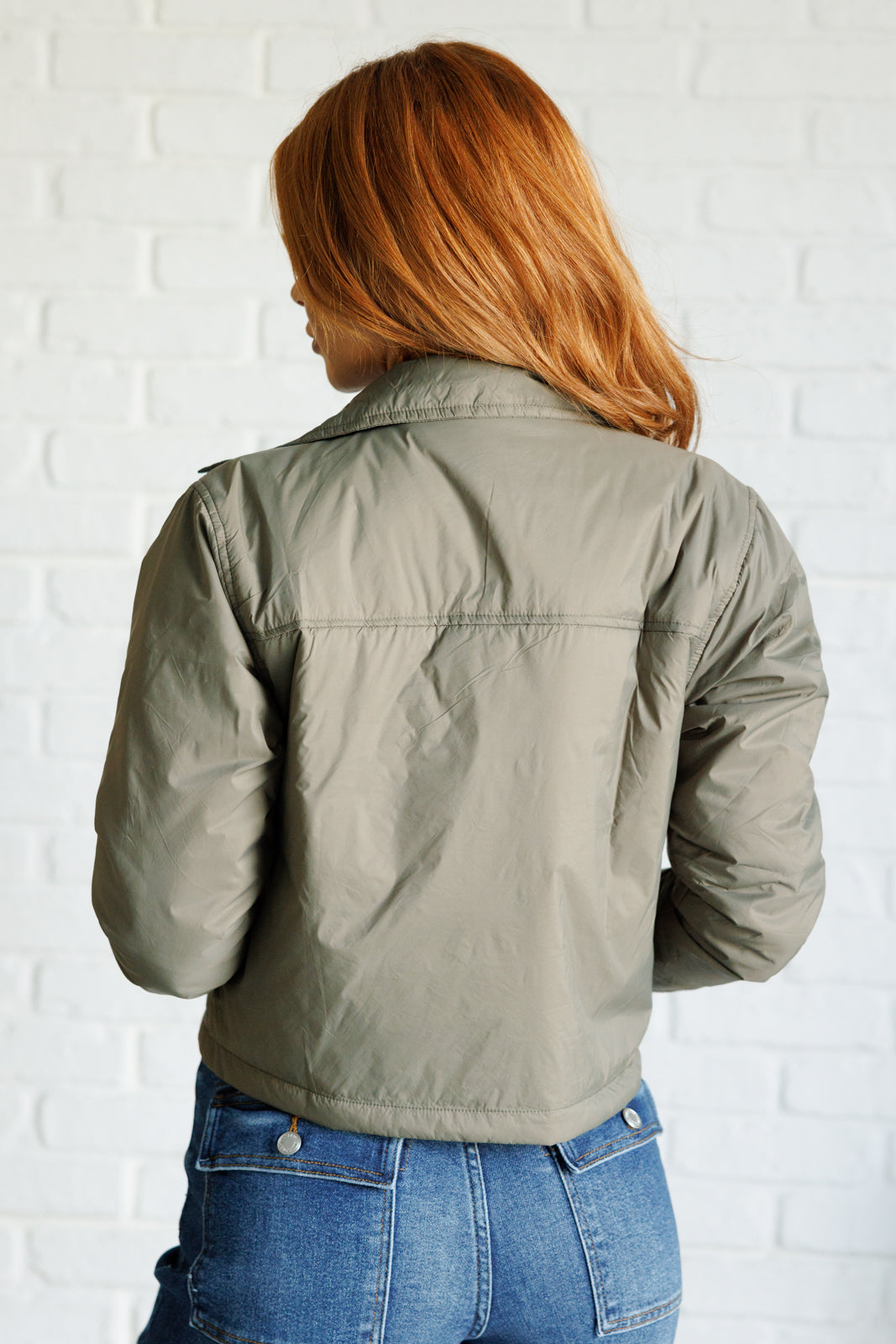 Olive lightweight puffer jacket with a collared neckline, long sleeves, snap front closure, cropped length, patch pockets, and a boxy silhouette.