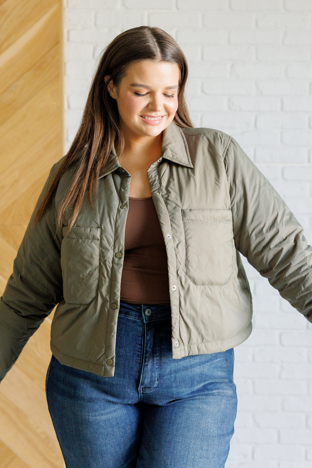 Olive lightweight puffer jacket with a collared neckline, long sleeves, snap front closure, cropped length, patch pockets, and a boxy silhouette.