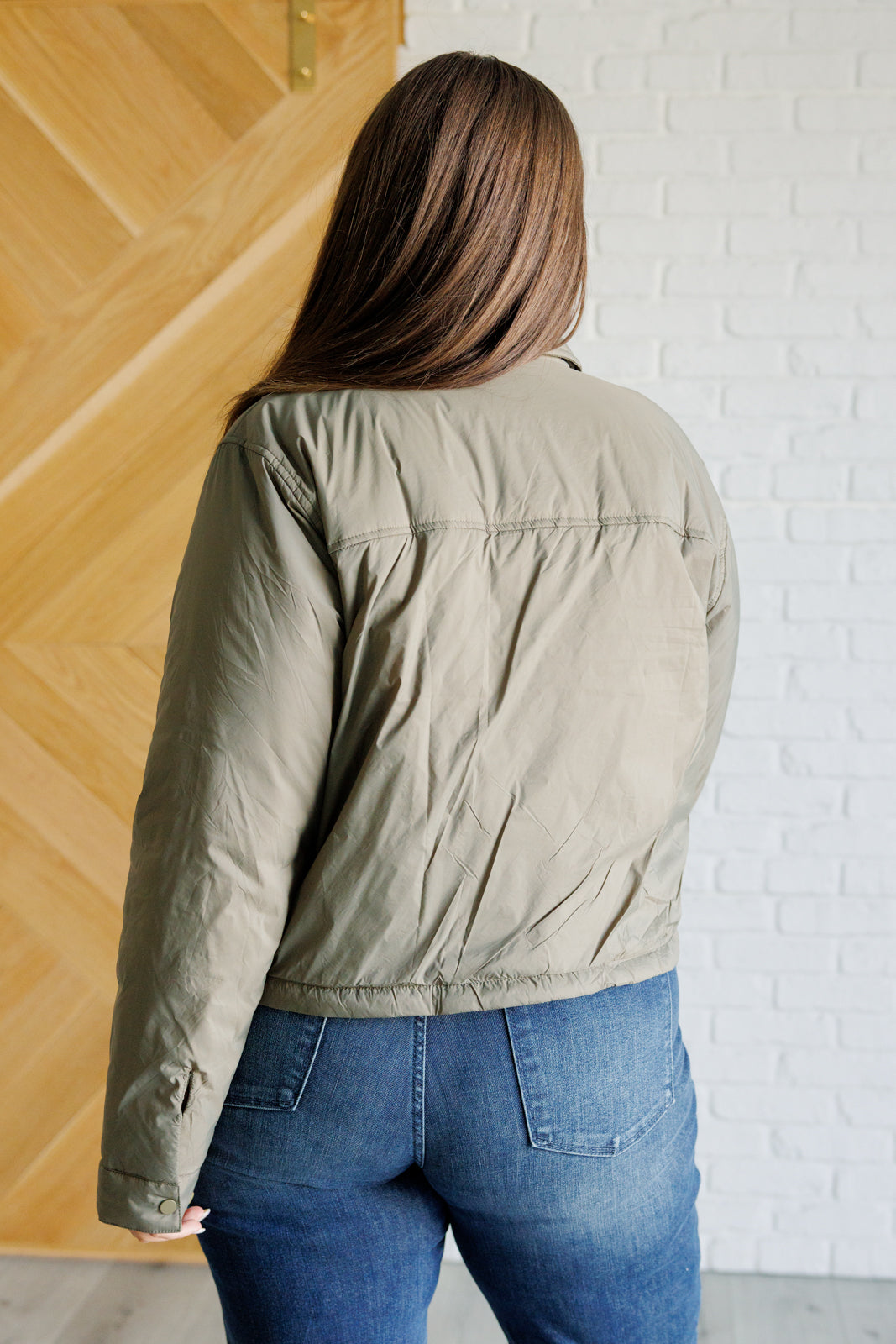 Olive lightweight puffer jacket with a collared neckline, long sleeves, snap front closure, cropped length, patch pockets, and a boxy silhouette.