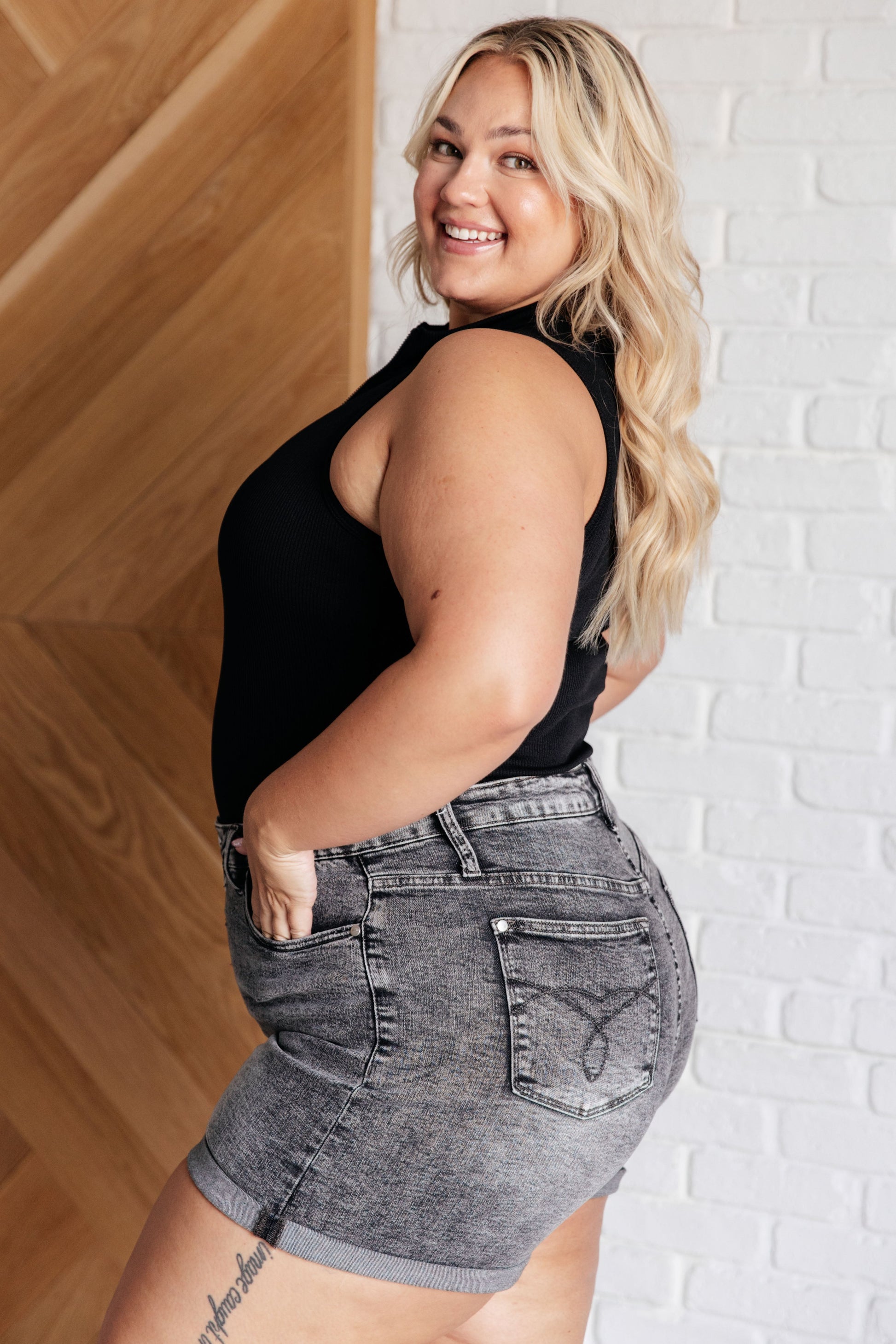 Side view of plus size Marley Ribbed Zip Up Bodysuit in black, featuring ribbed knit fabric, mock neckline, and half zip closure.