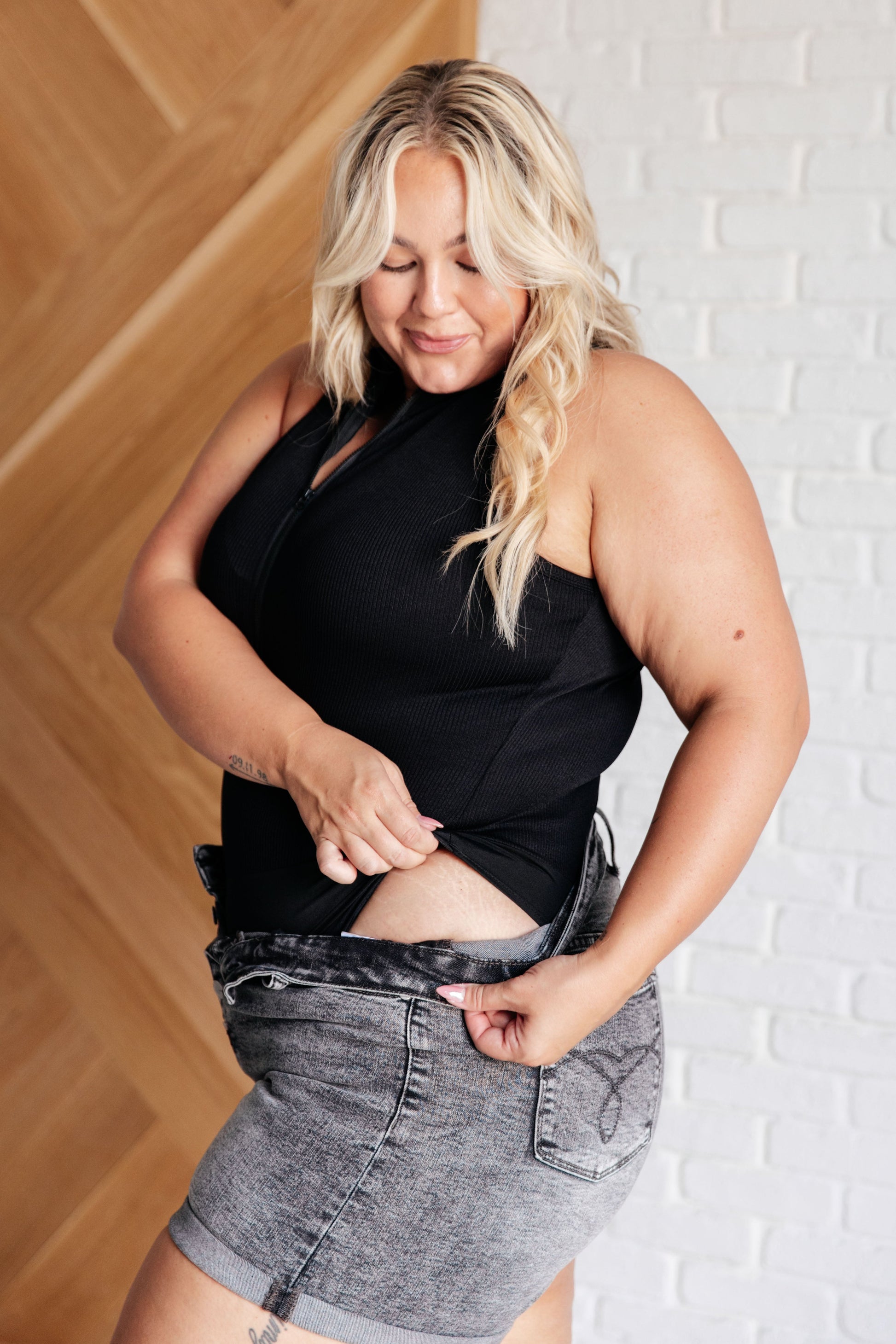 Side view of plus size woman wearing the Marley Ribbed Zip Up Bodysuit in black.
